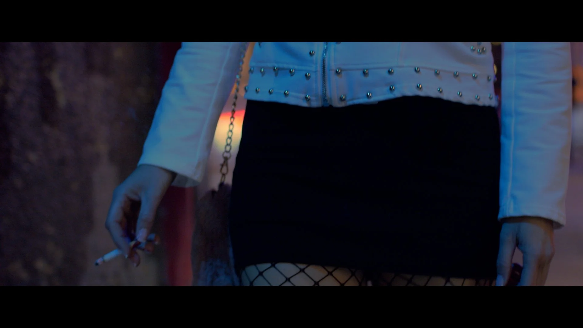 Persona con chaqueta de tachuelas y falda corta con medias de red, sosteniendo un cigarrillo.