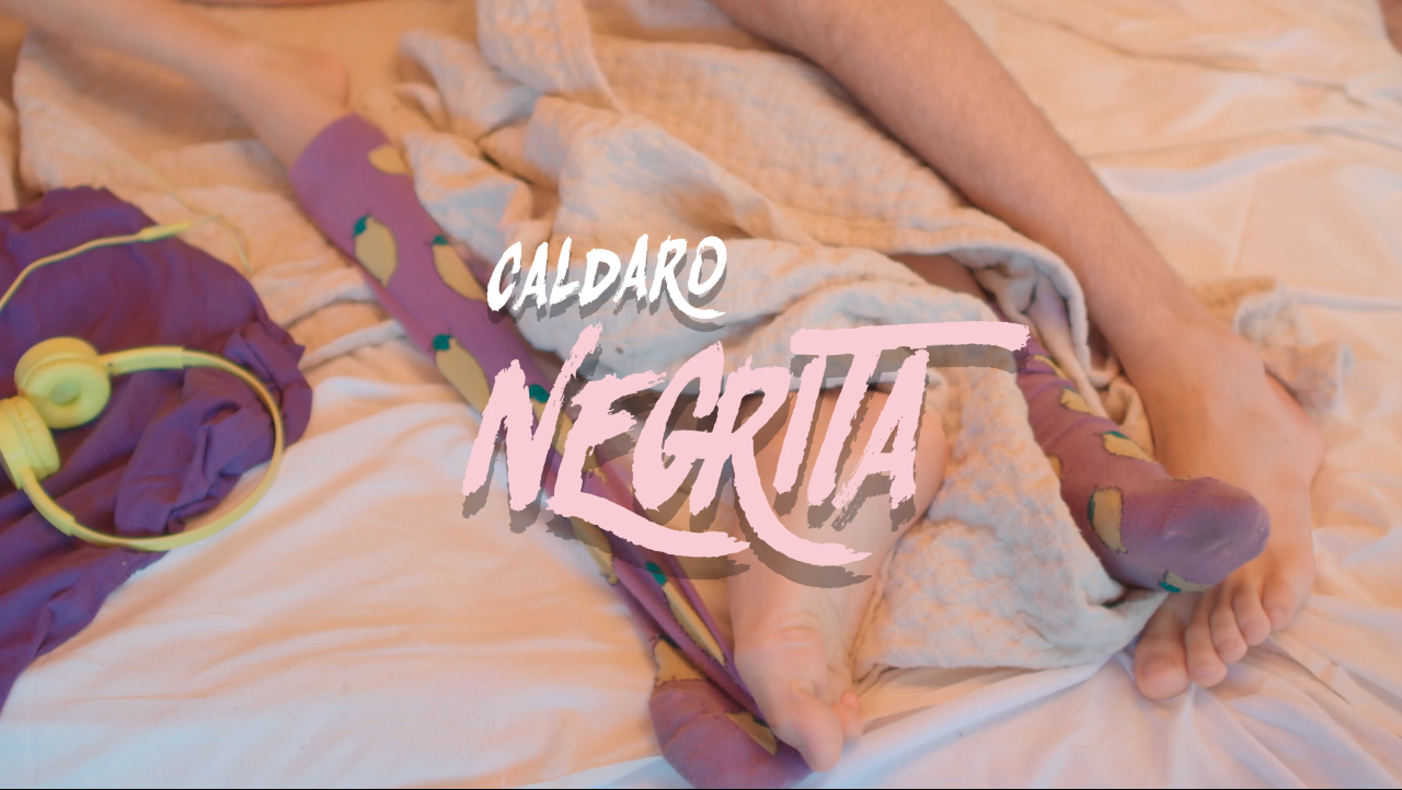 Una persona acostada en una cama con un calcetín de color púrpura con figuras de limones y una cubierta con una mano visible. También hay auriculares amarillos junto a la persona.