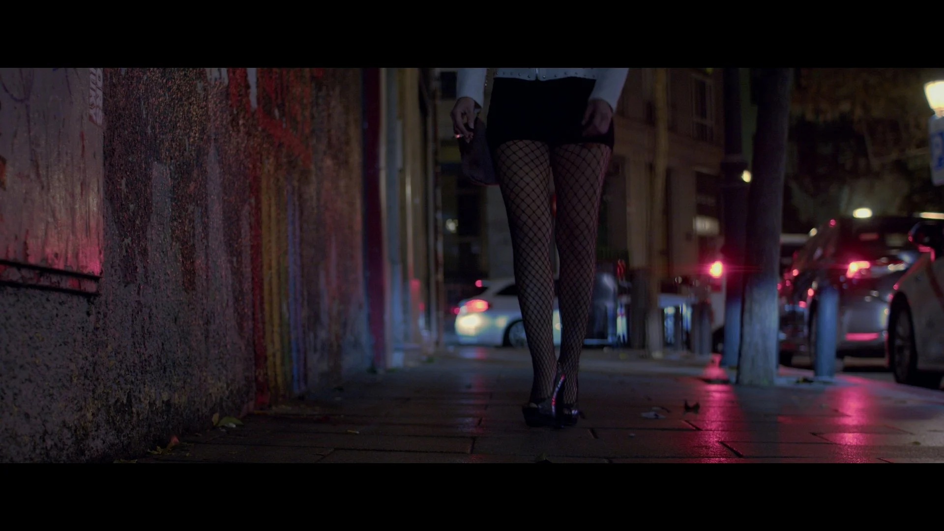 Mujer caminando por la calle en la noche, viste medias de red y tacones altos.