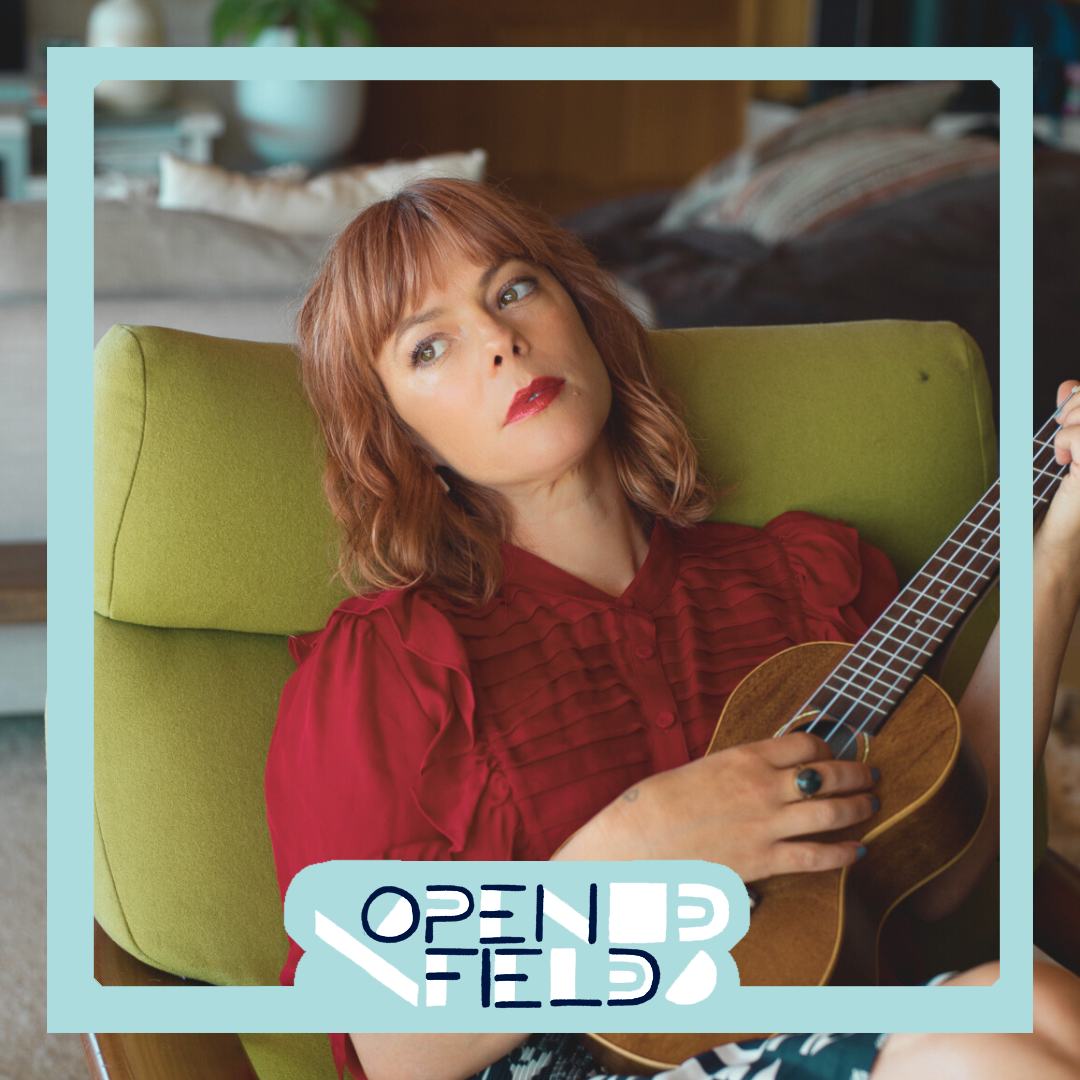 Person sitting in a green chair holding a ukulele, with a contemplative expression, wearing a red blouse. The frame is labeled 'Open Field.'