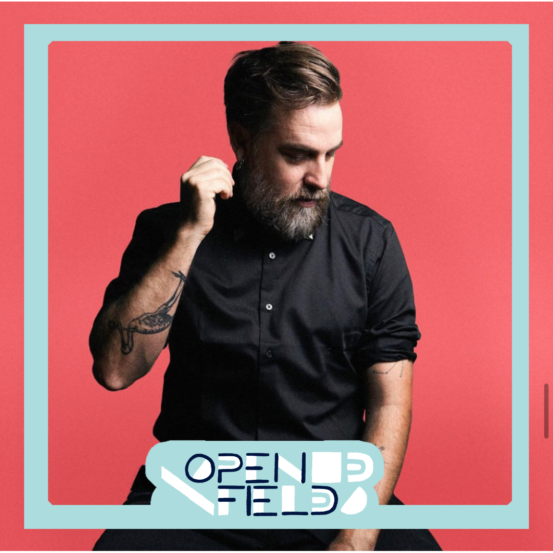 Man with tattoos in black shirt against pink background, blue frame with "Open Field" text.