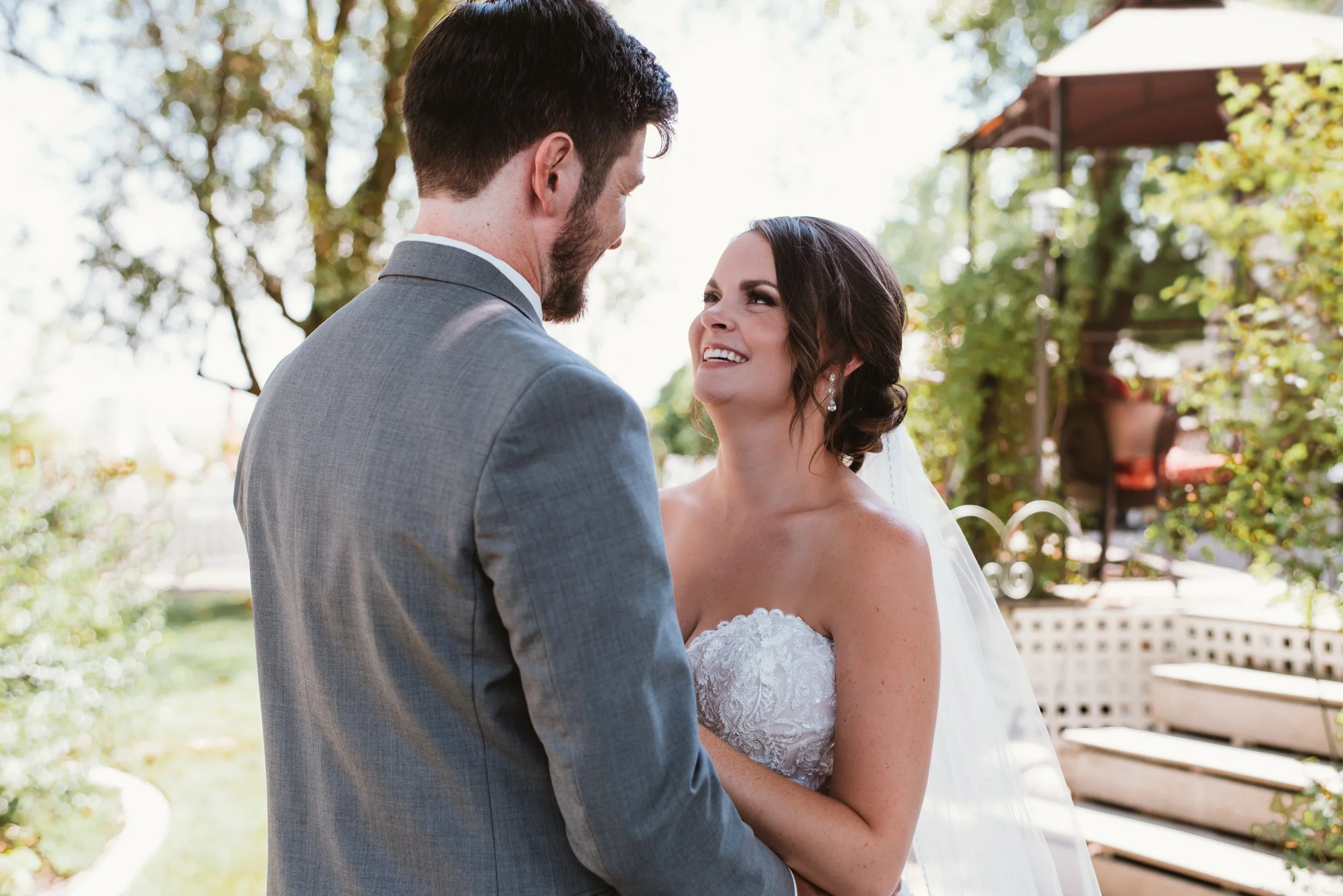 A bride and groom smiling at each other outdoors on their wedding day.