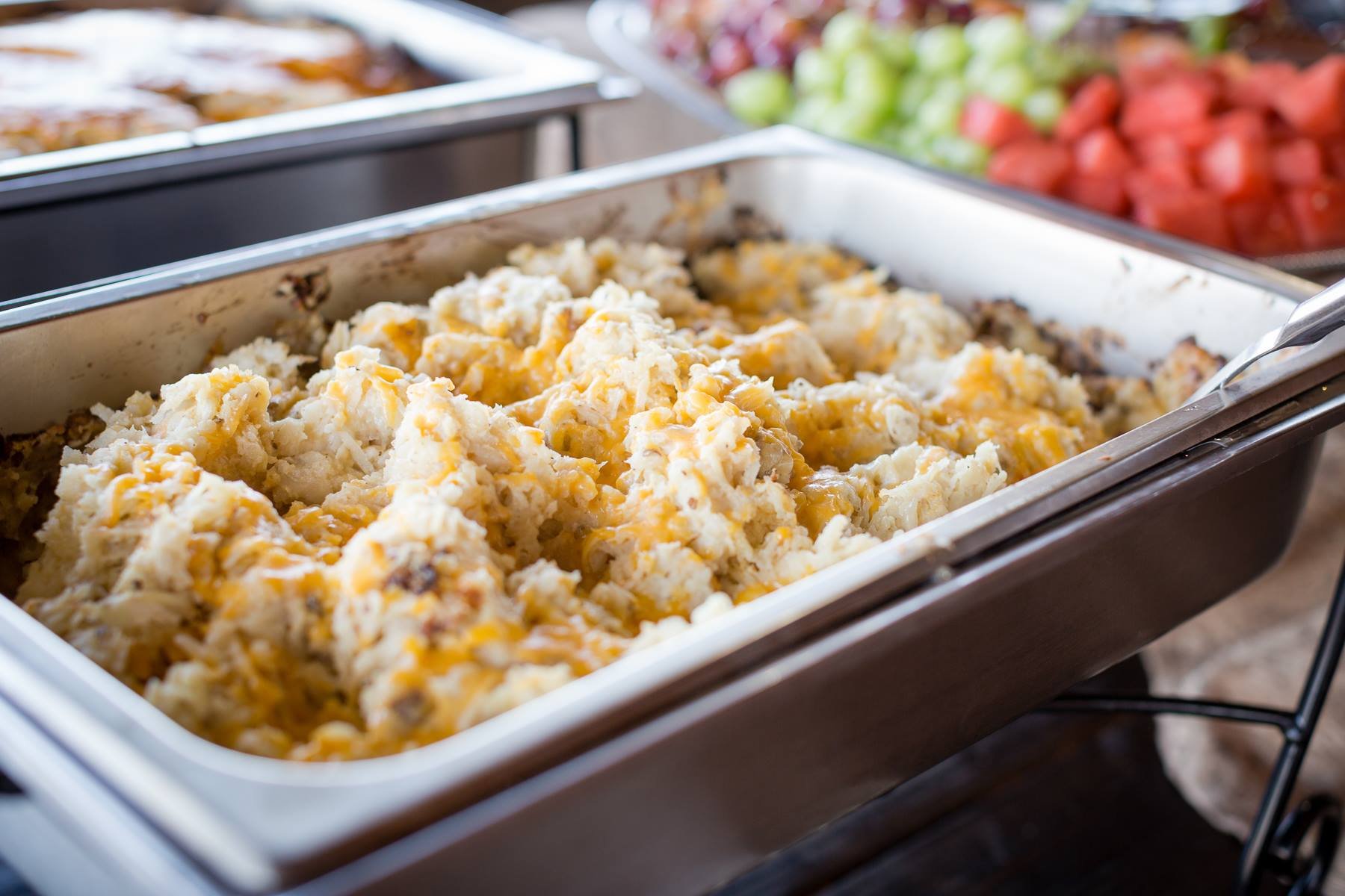 Chafing dish with mashed potatoes topped with cheese in a buffet setting.