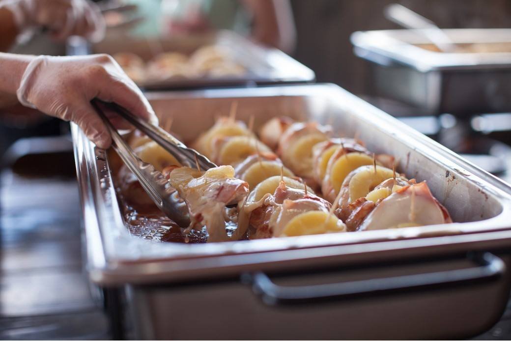 Person serving bacon-wrapped pineapple skewers from a catering tray.