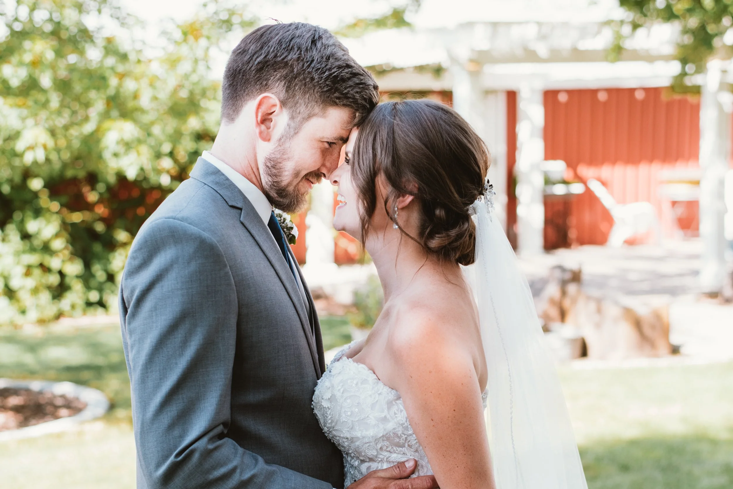 Bride and groom touching foreheads in wedding attire outside.