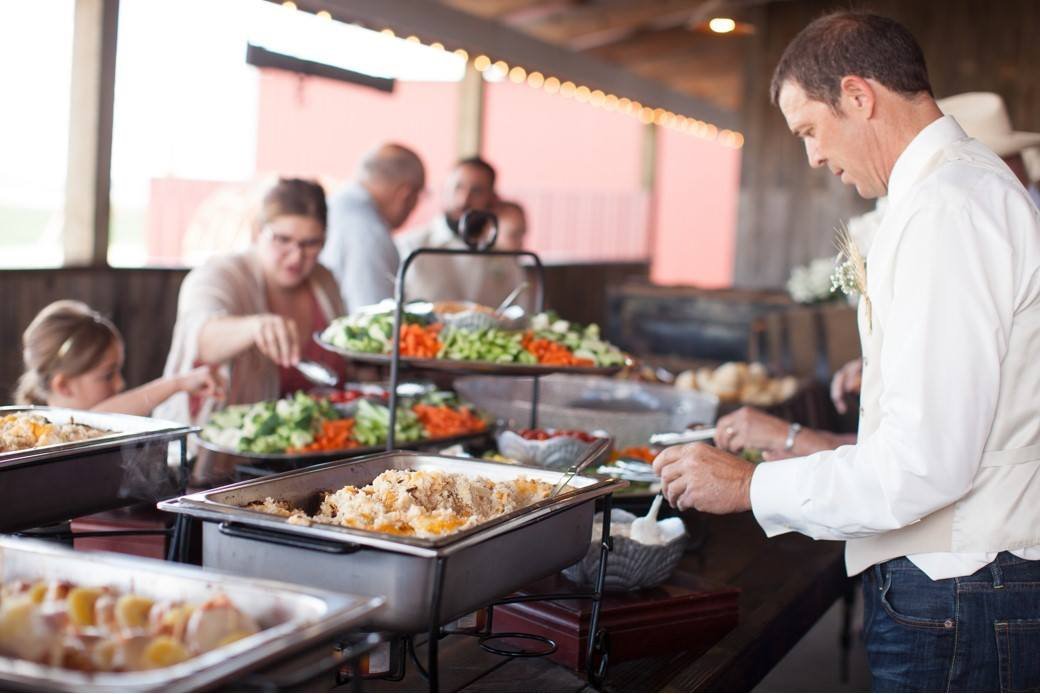 Buffet table with food trays, people serving themselves at an event.