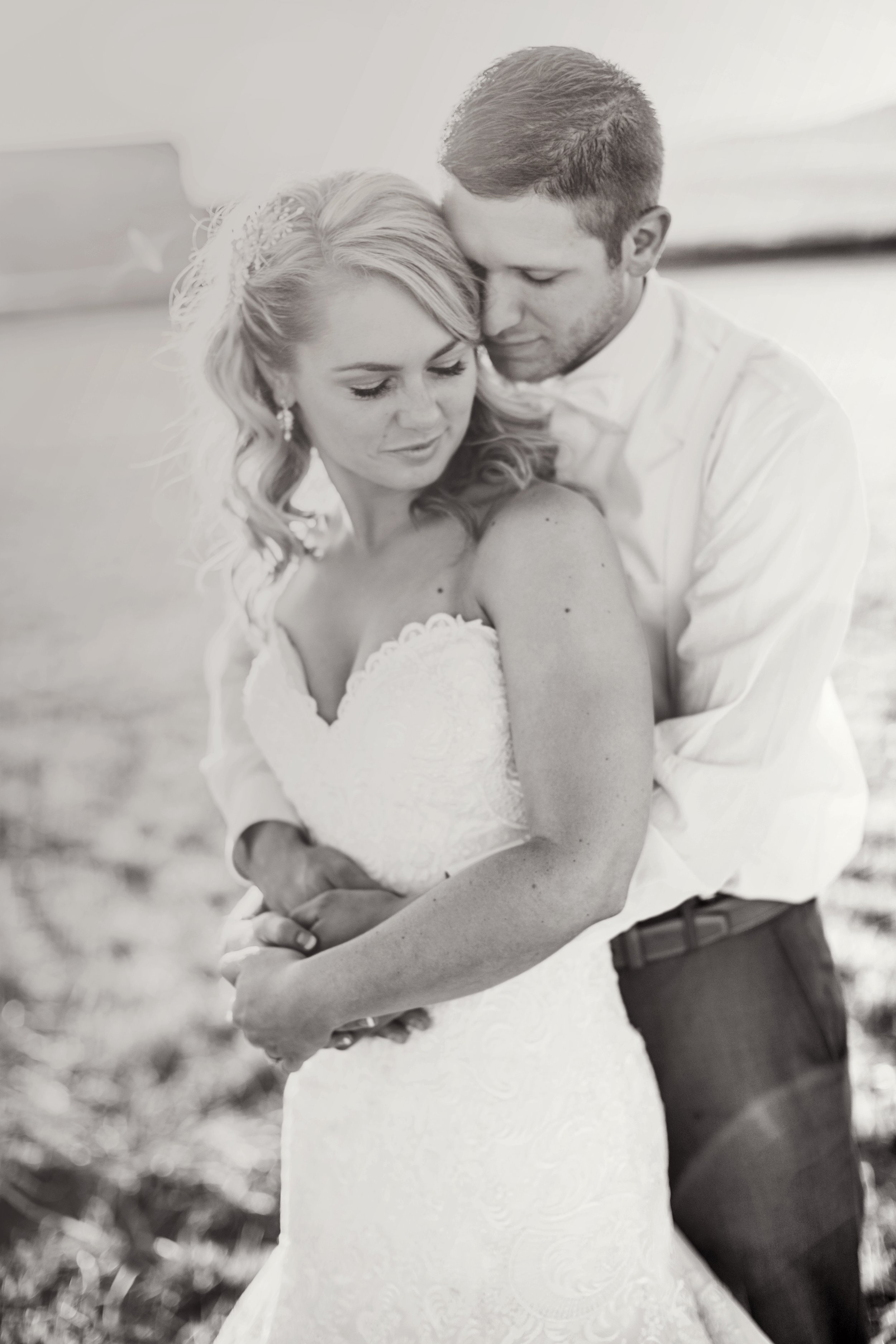 Black and white photo of a groom embracing a bride in a wedding dress outdoors.