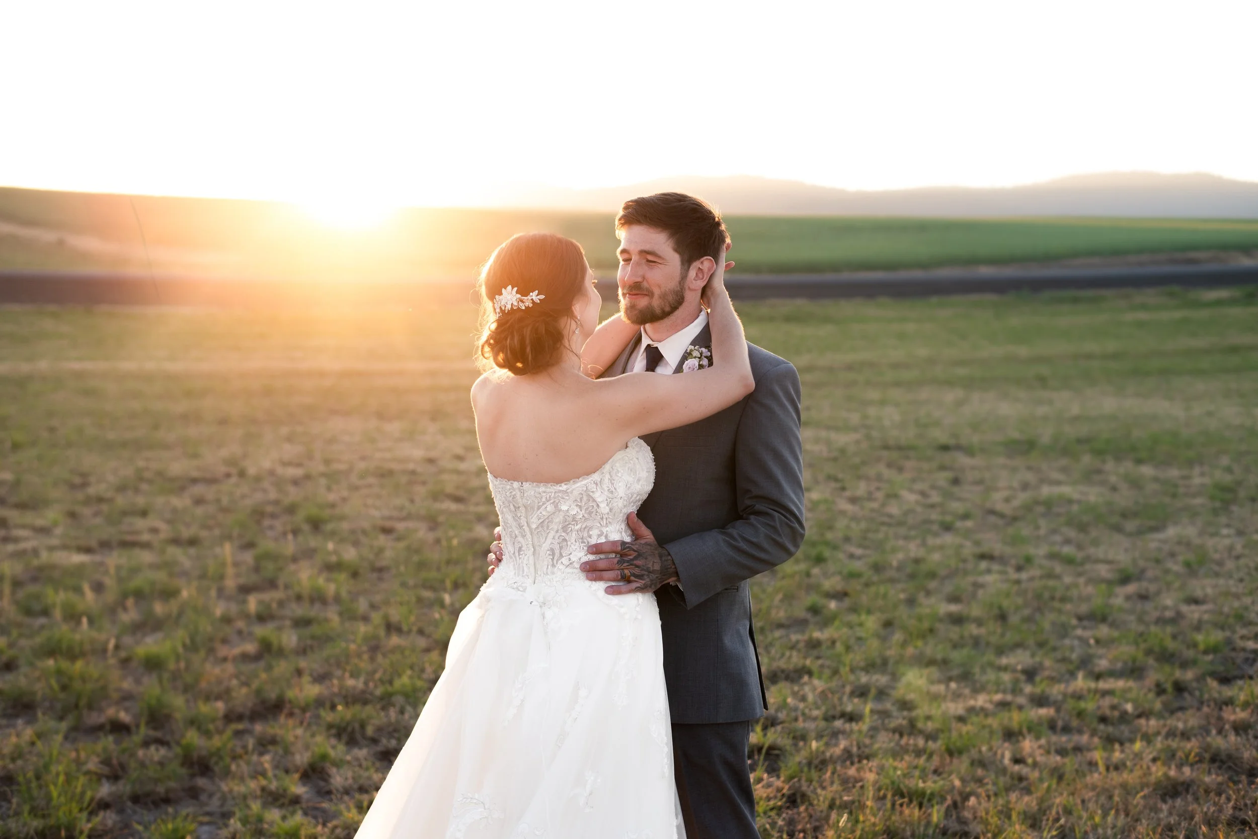 Bride and groom embracing in a field at sunset