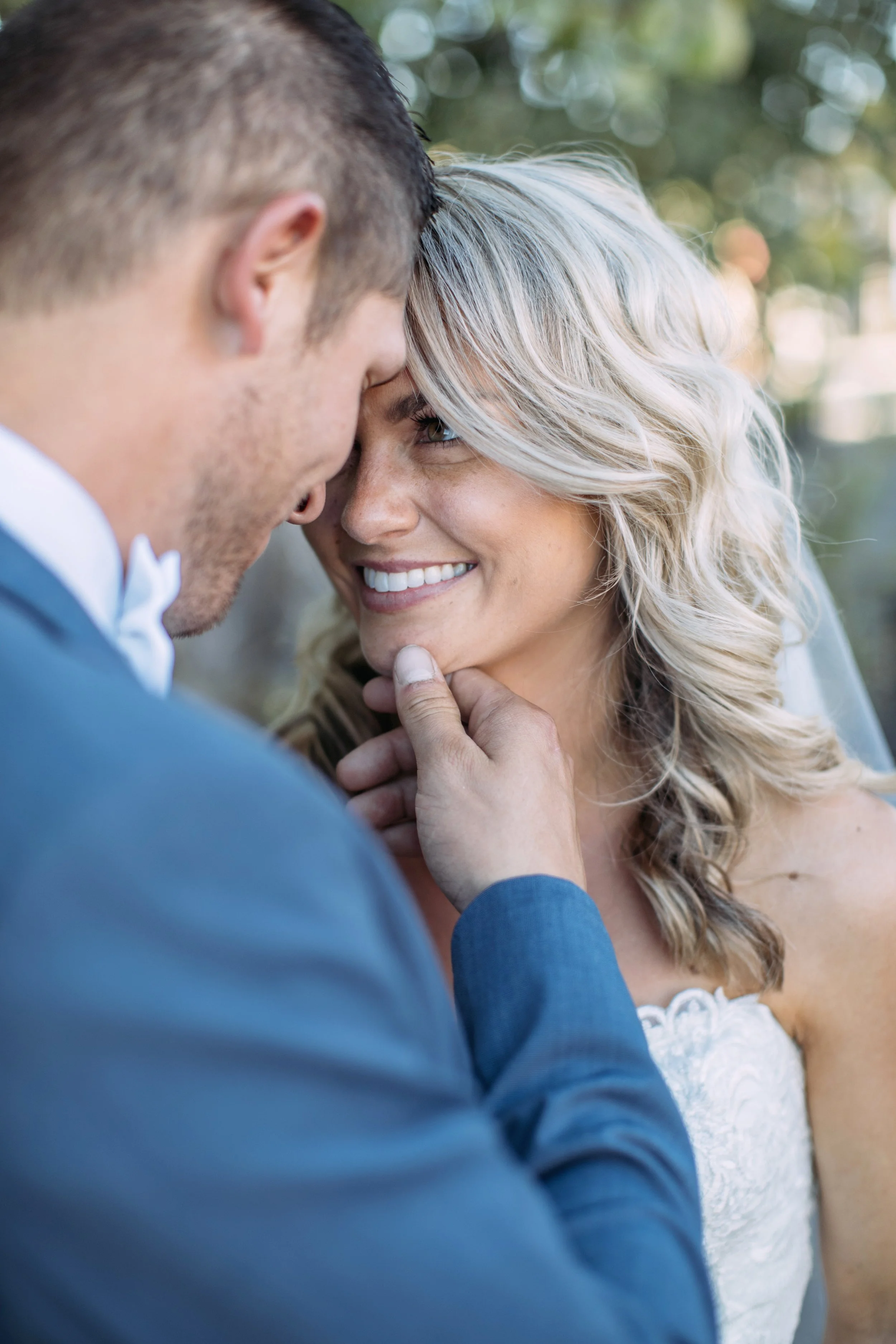 Close-up of a couple embracing outdoors, the man in a suit gently touching the woman's face, both smiling.