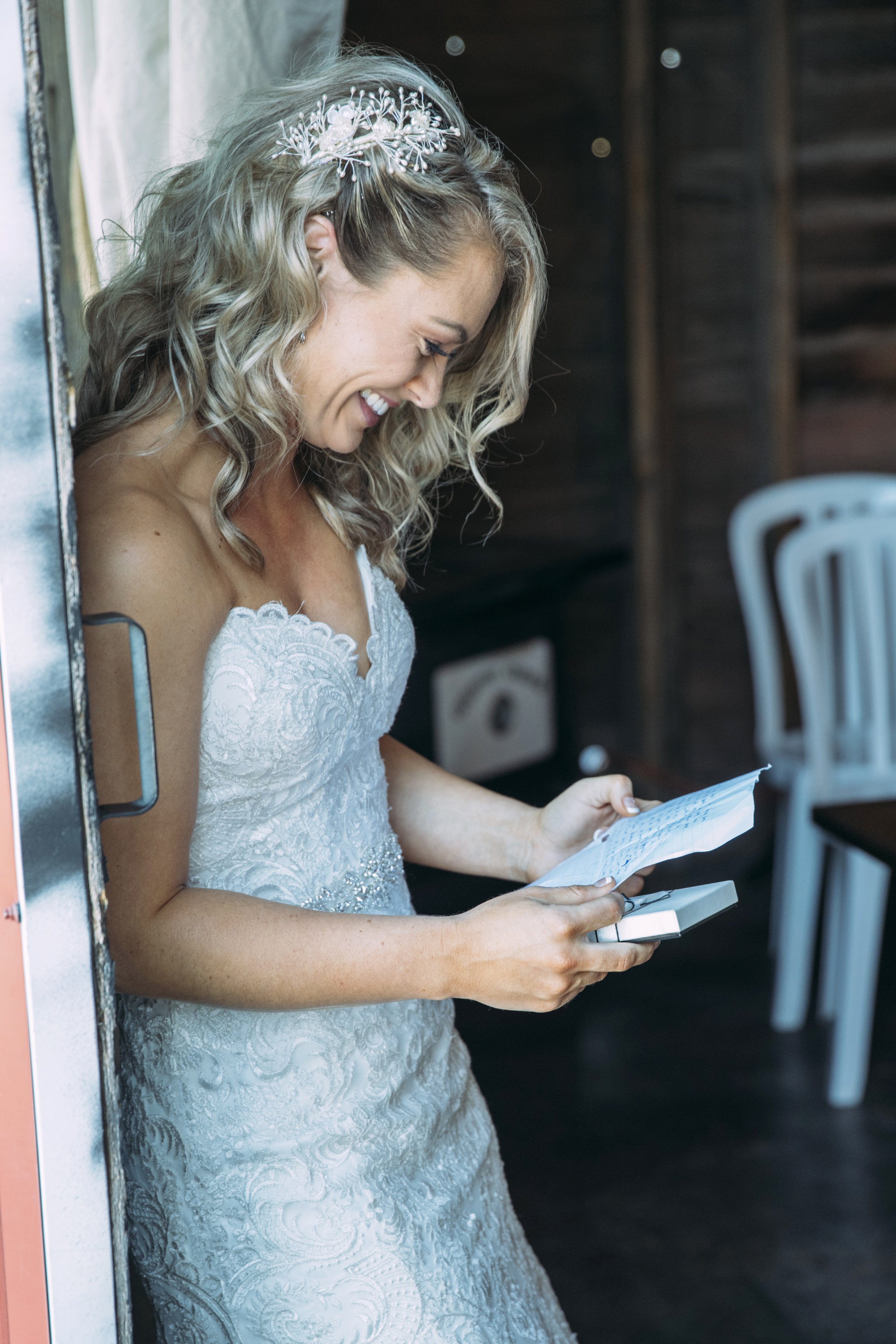 Smiling bride in a white wedding dress holding a letter and a small box.