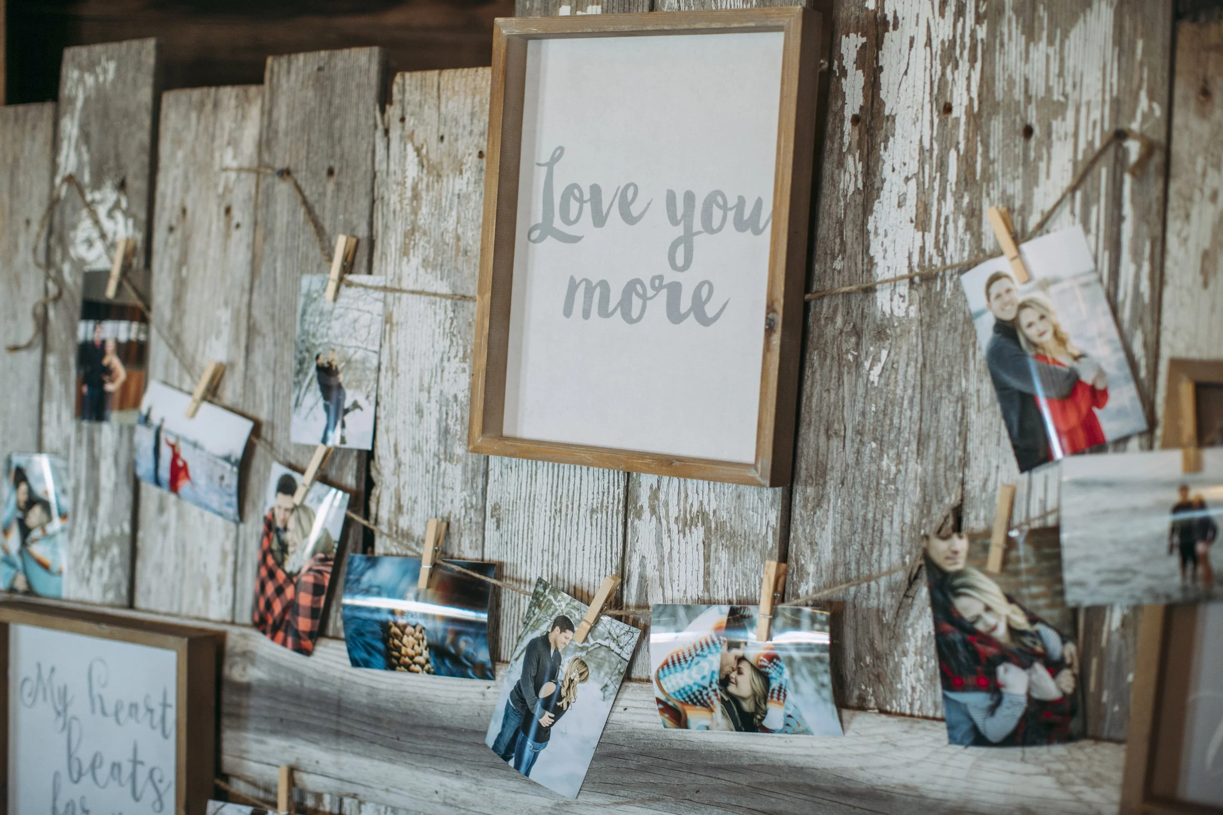 Rustic wooden wall with a "Love you more" sign and multiple photos clipped to twine.