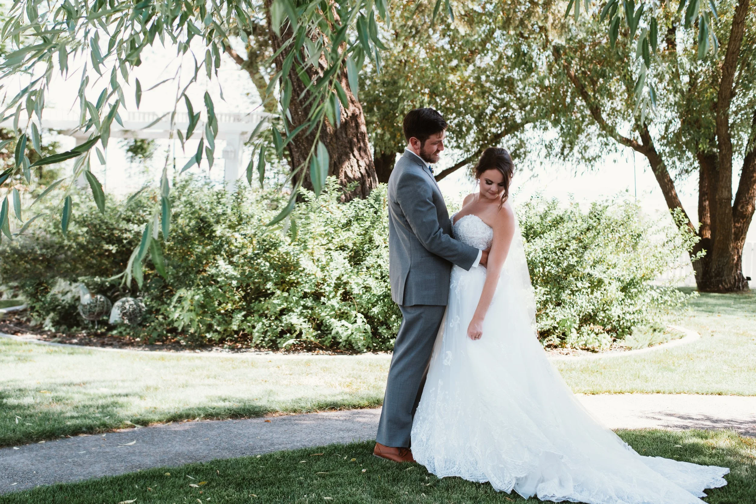 Bride and groom embracing outdoors near trees and bushes.