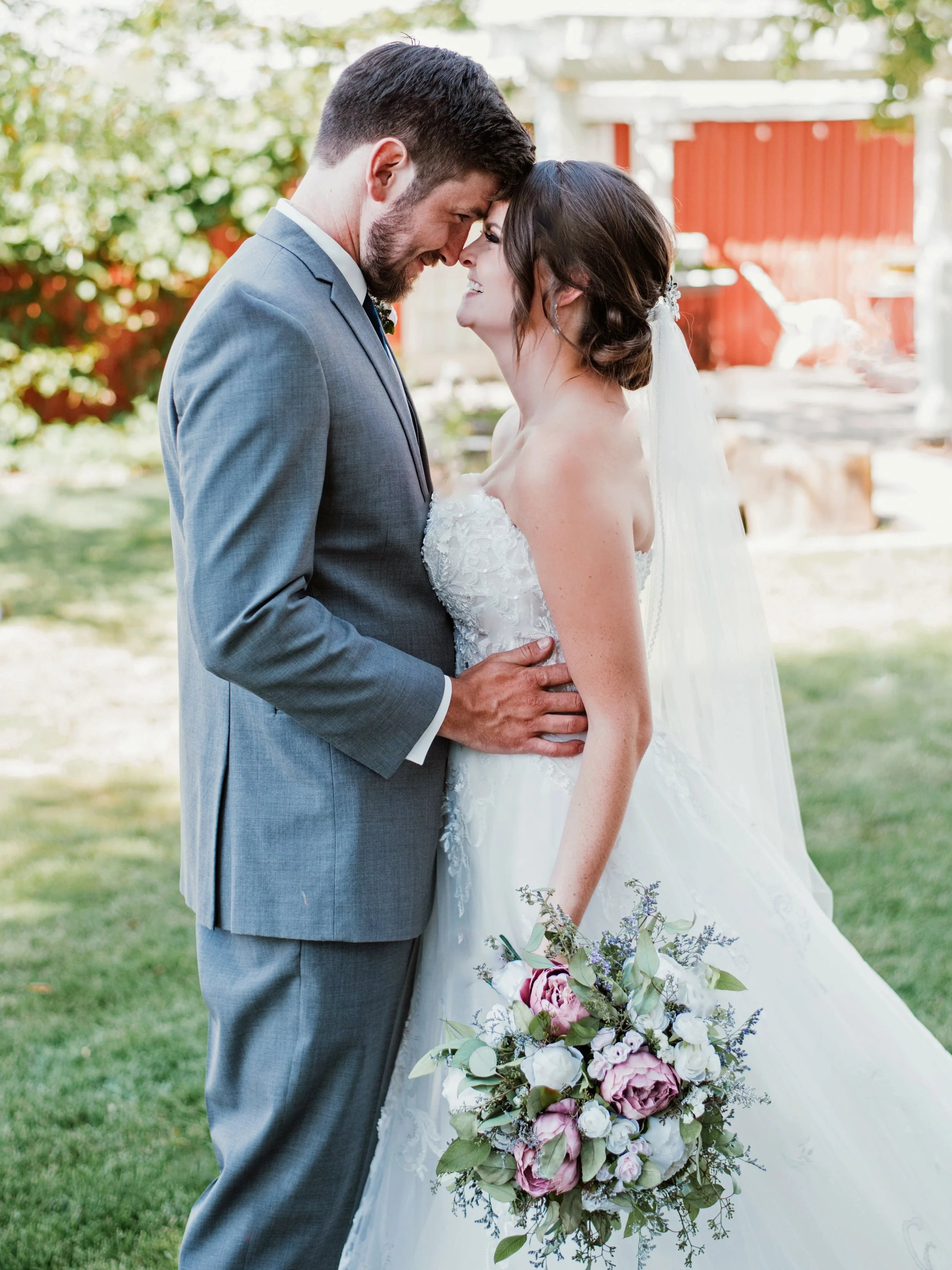 Bride and groom embracing outdoors, bride holding bouquet, wearing wedding attire.