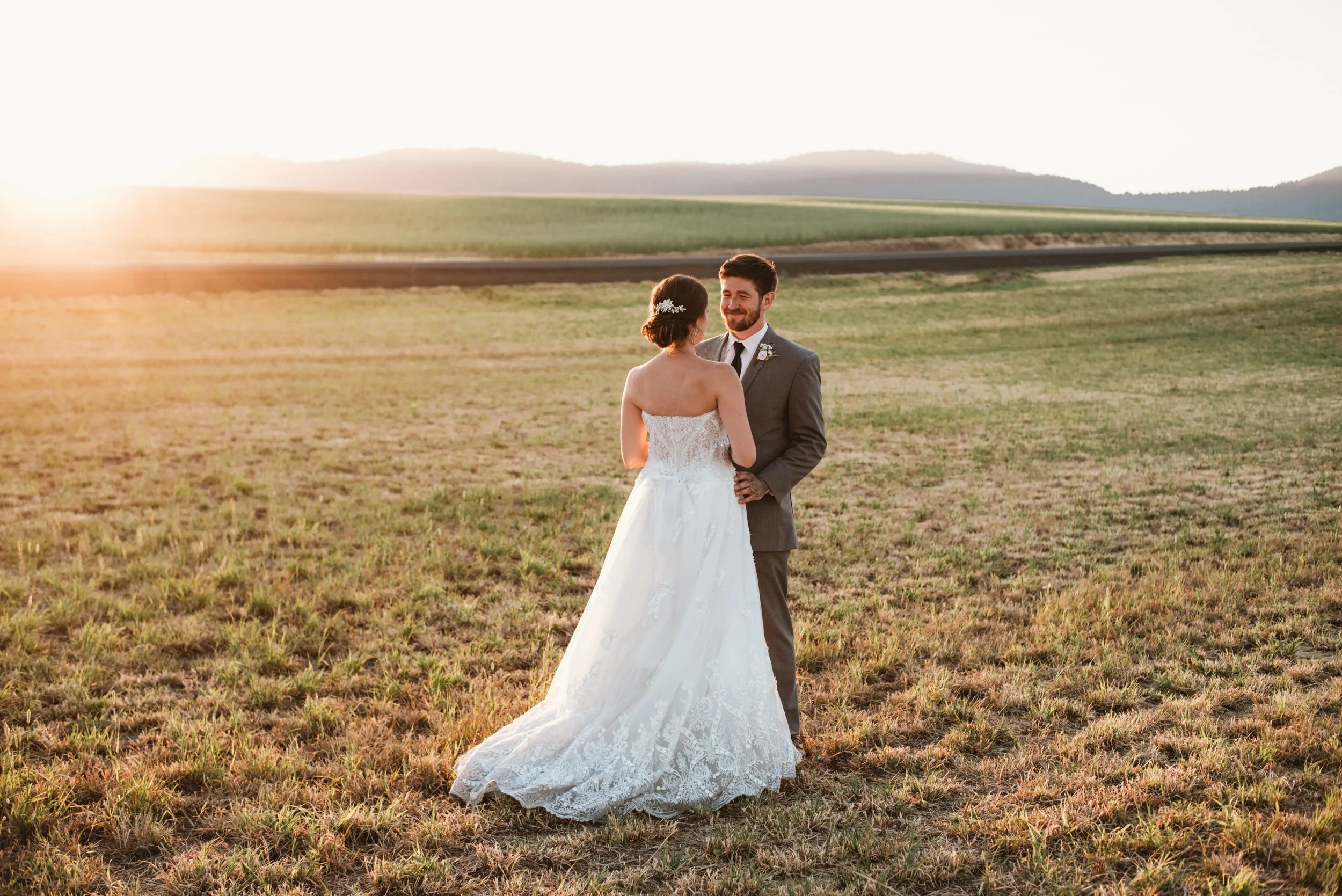 Bride and groom in a field at sunset with mountains in the background.