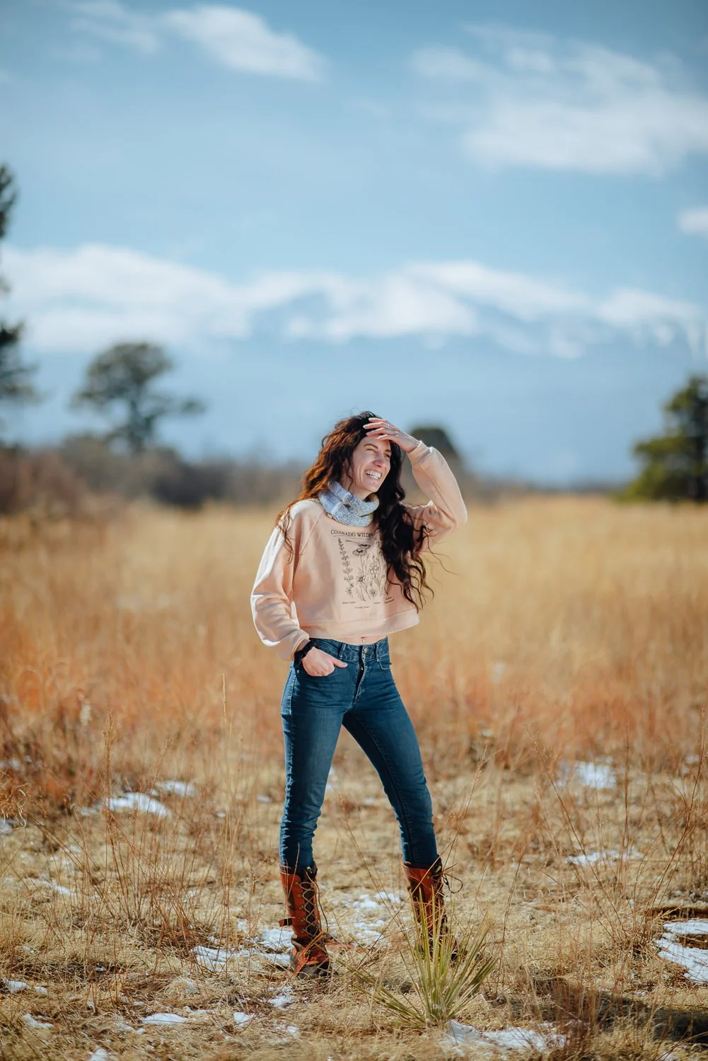 Lifestyle photography of a model with long dark wavy hair wearing a peach wildflower crewneck sweater at Palmer Park in Colorado Springs, Colorado for Akinz Boardwear