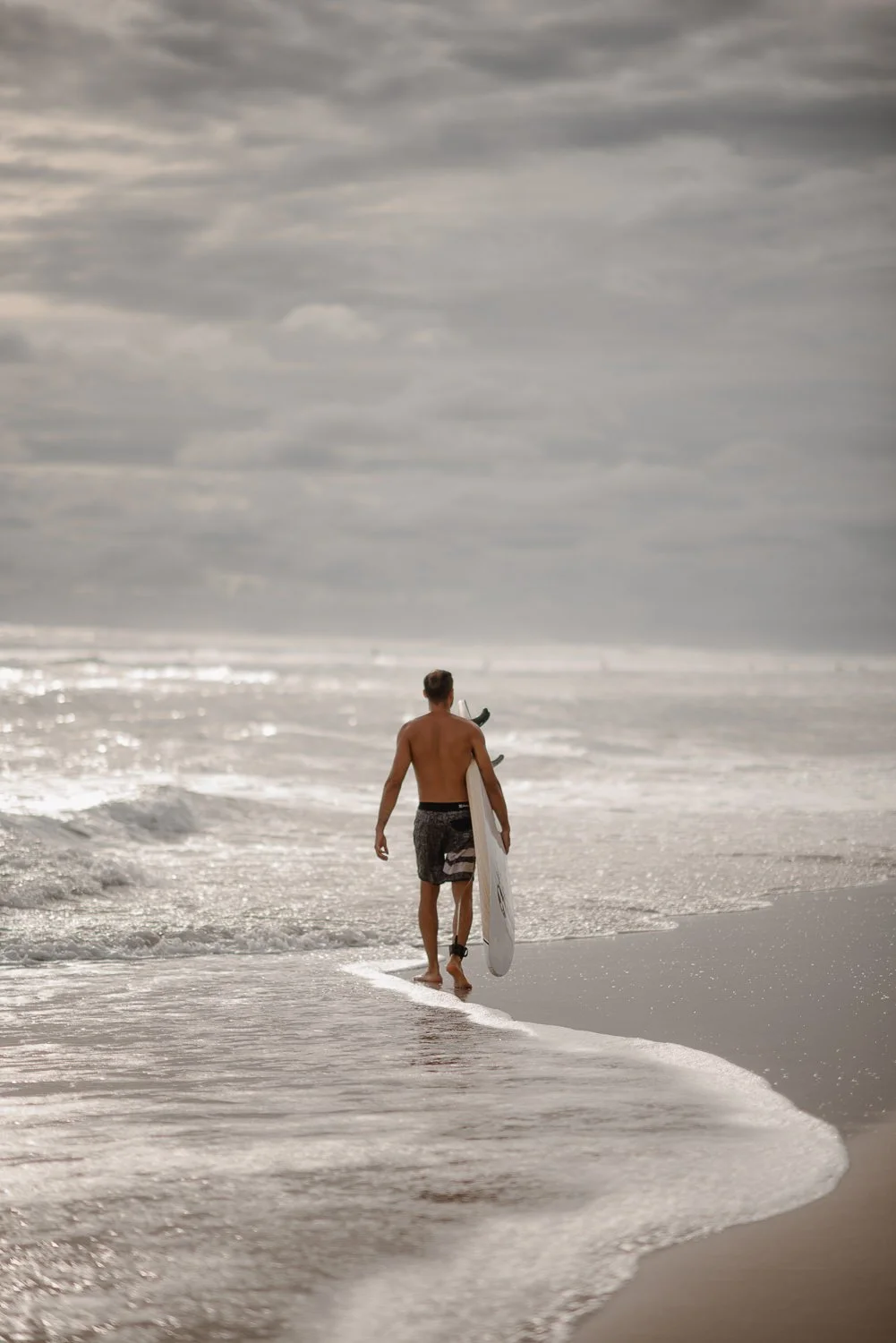 Travel image of a surfer walking into the ocean on an overcast sunset in Santa Teresa, Costa Rica