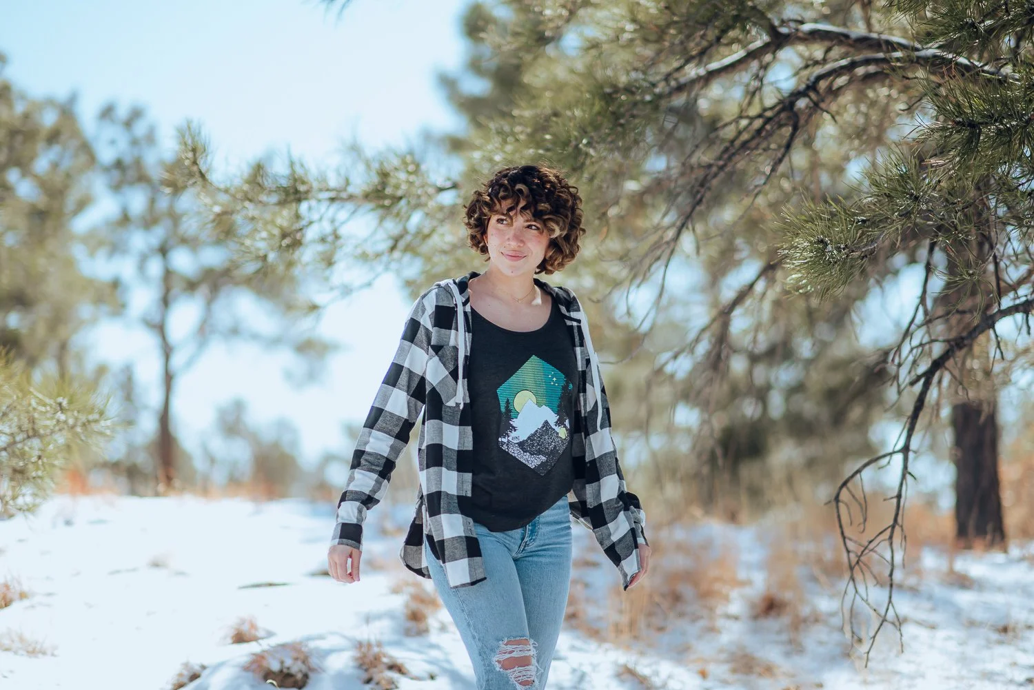 Professional lifestyle photography of young Puerto Rican model with short, curly, brown hair wearing Akinz Boardwear clothing in the snowy mountains in Colorado Springs, Colorado
