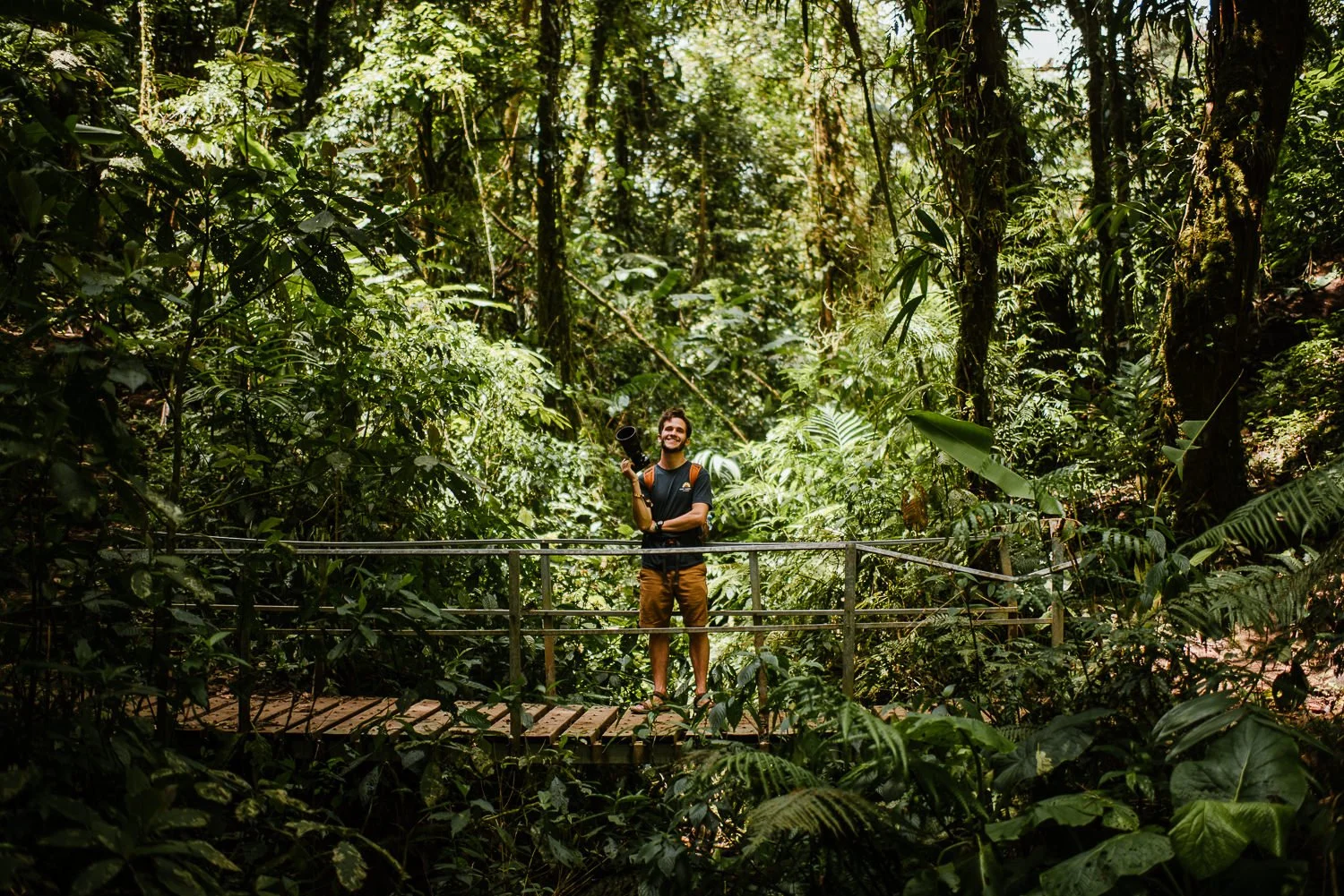 travel photography of a photographer smiling on a bridge near a trail in Monteverde cloud forest in Costa Rica