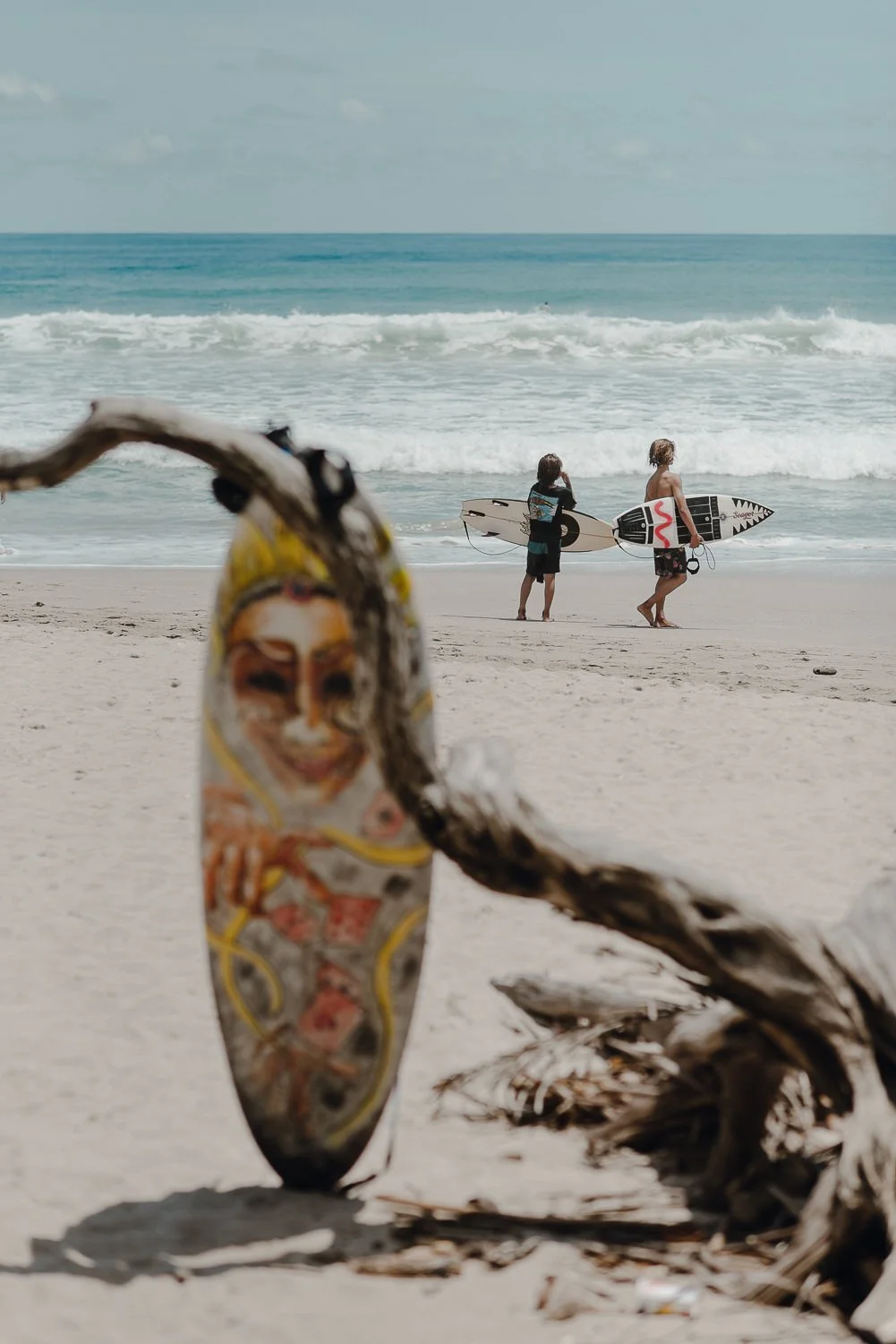 Unique lifestyle photography of young surfers on the beach with a surfboard resting on driftwood in the foreground
