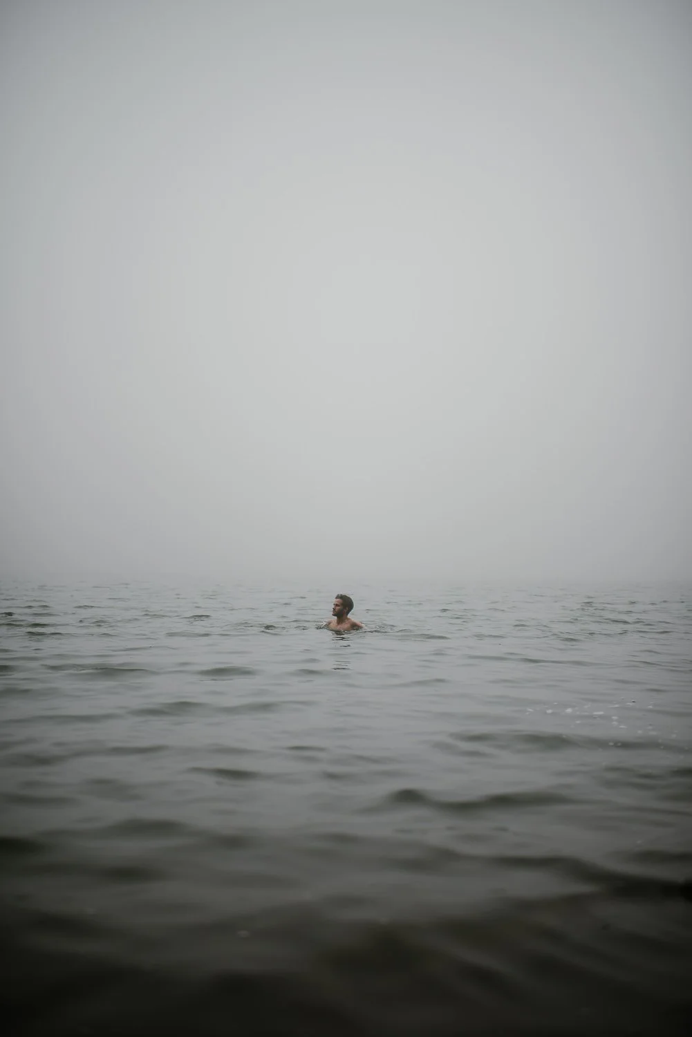 Travel portrait photograph of a young man swimming in the foggy lake at the top of Cerro Chato in Costa Rica