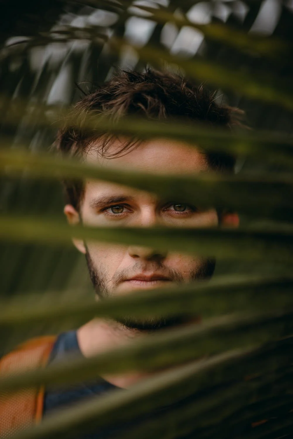 Travel portrait photograph of a young man behind a palm leaf
