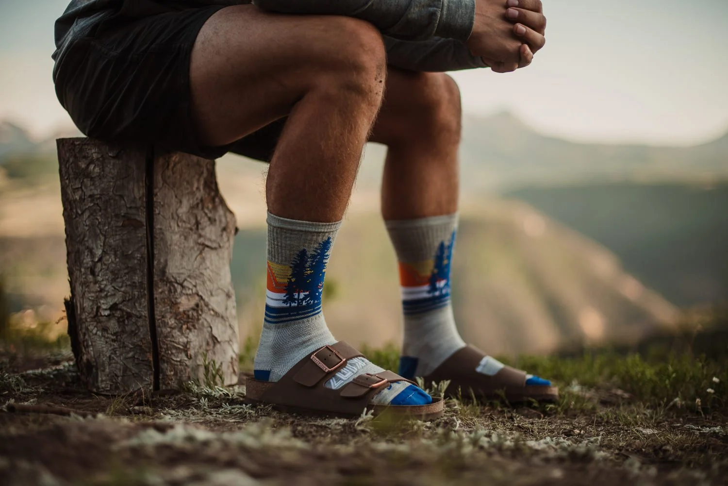Outdoor product photography of a man sitting on a log, wearing Akinz Boardwear gear in Telluride, CO.
