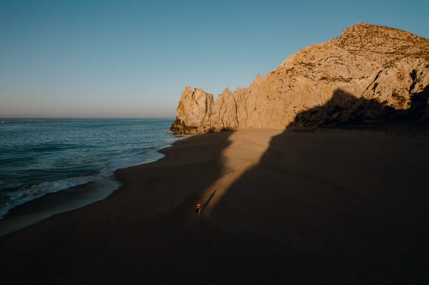 Travel drone photography of girl walking on the shore during golden hour sunrise at Divorce Beach in Cabo San Lucas, Mexico