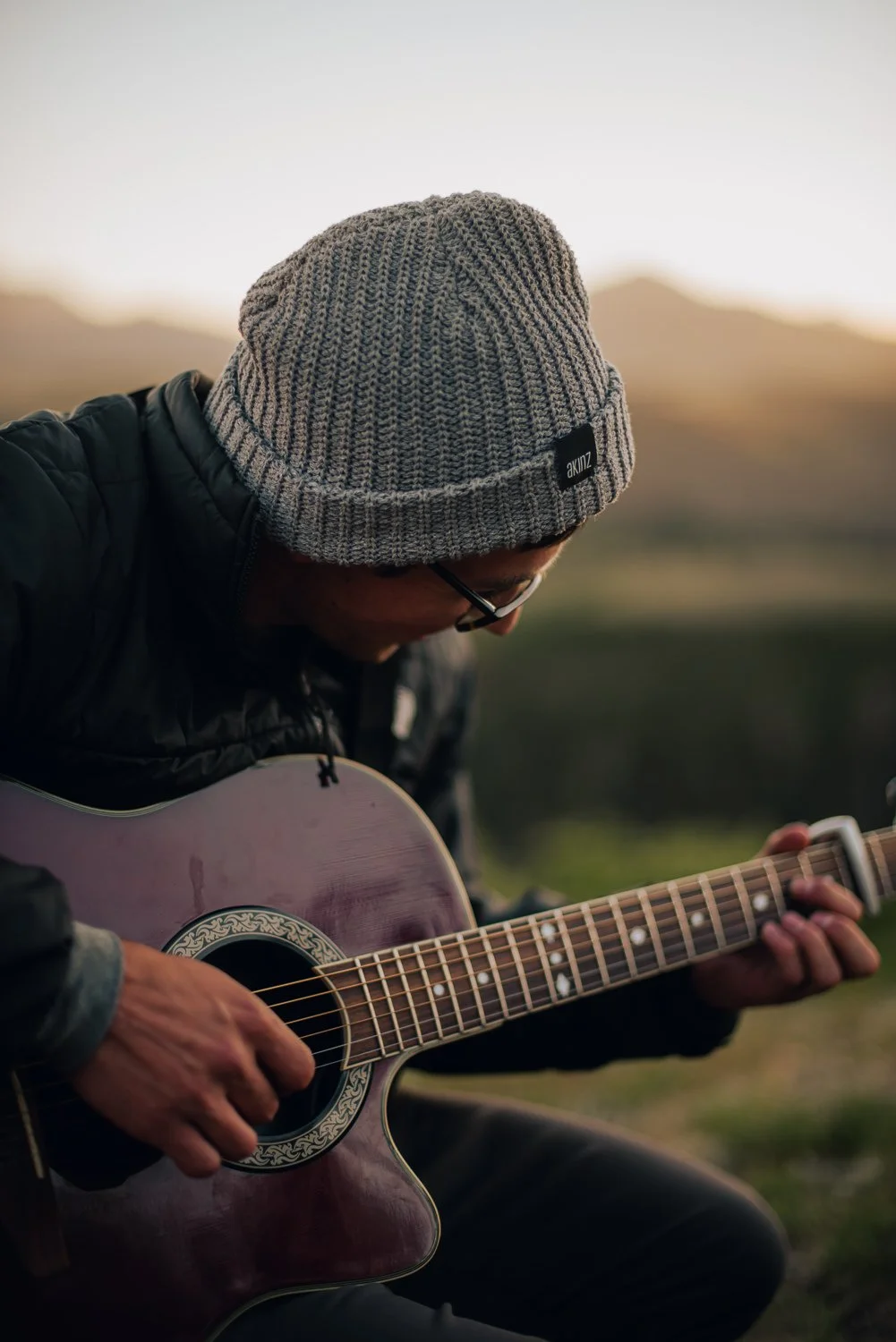 Outdoor product photography of a man playing guitar, wearing an Akinz Boardwear beanie while on a camping trip in the mountains in Telluride, CO.