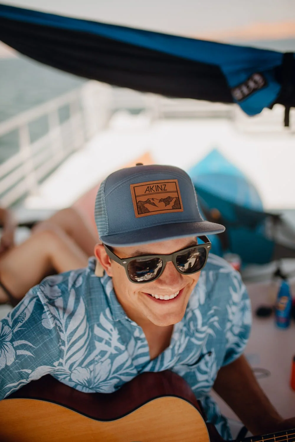 Adventure lifestyle photography of a guy wearing a blue Akinz snapback while playing guitar on a boat on Lake Powell in Utah