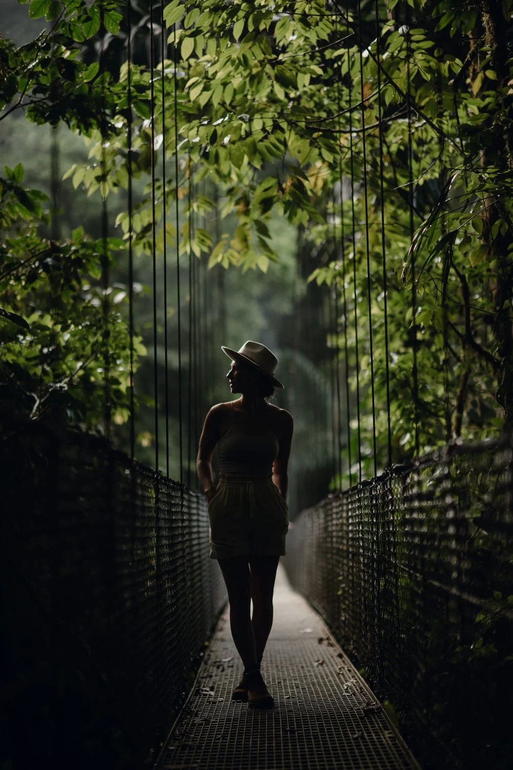 Lifestyle portrait of a girl wearing a hat, walking on a hanging bridge in the cloud forest in La Fortuna, Costa Rica