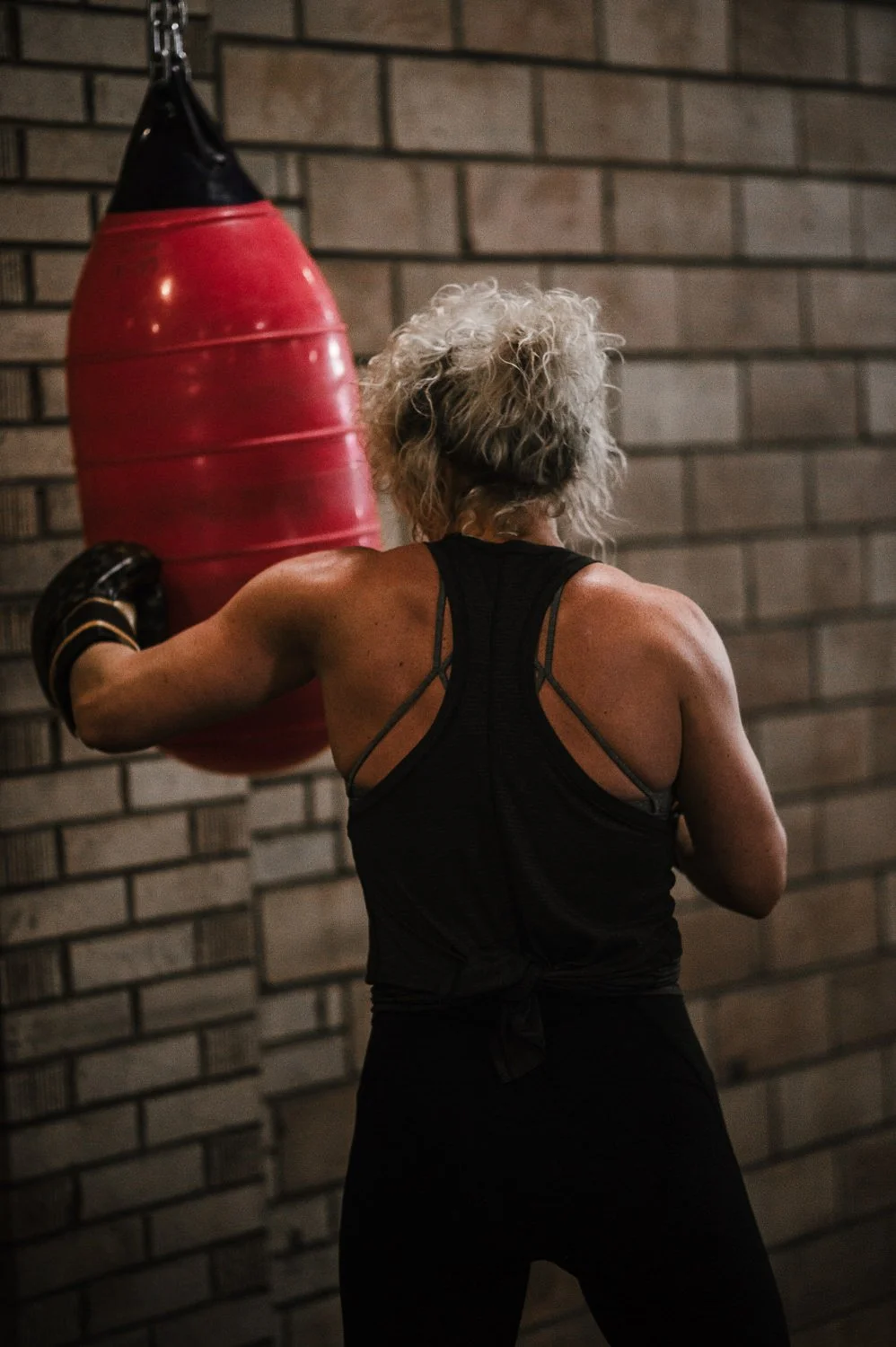 Lifestyle fitness photograph of a woman hitting a punching bag at Beautifully Savage boutique boxing gym in Fort Collins, Colorado