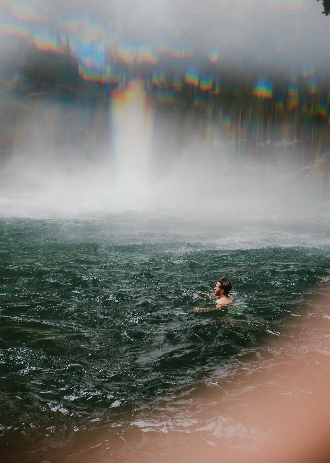 Travel photograph of a young man swimming in the base of La Fortuna waterfall