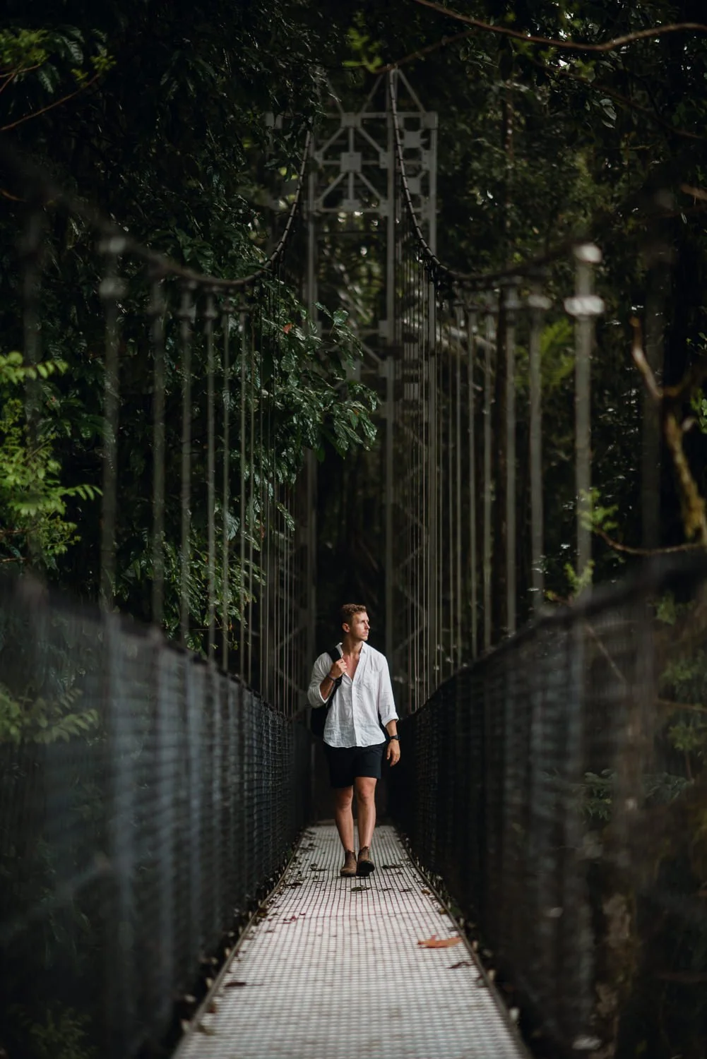 Lifestyle portrait of a guy walking on a hanging bridge in the cloud forest in La Fortuna, Costa Rica
