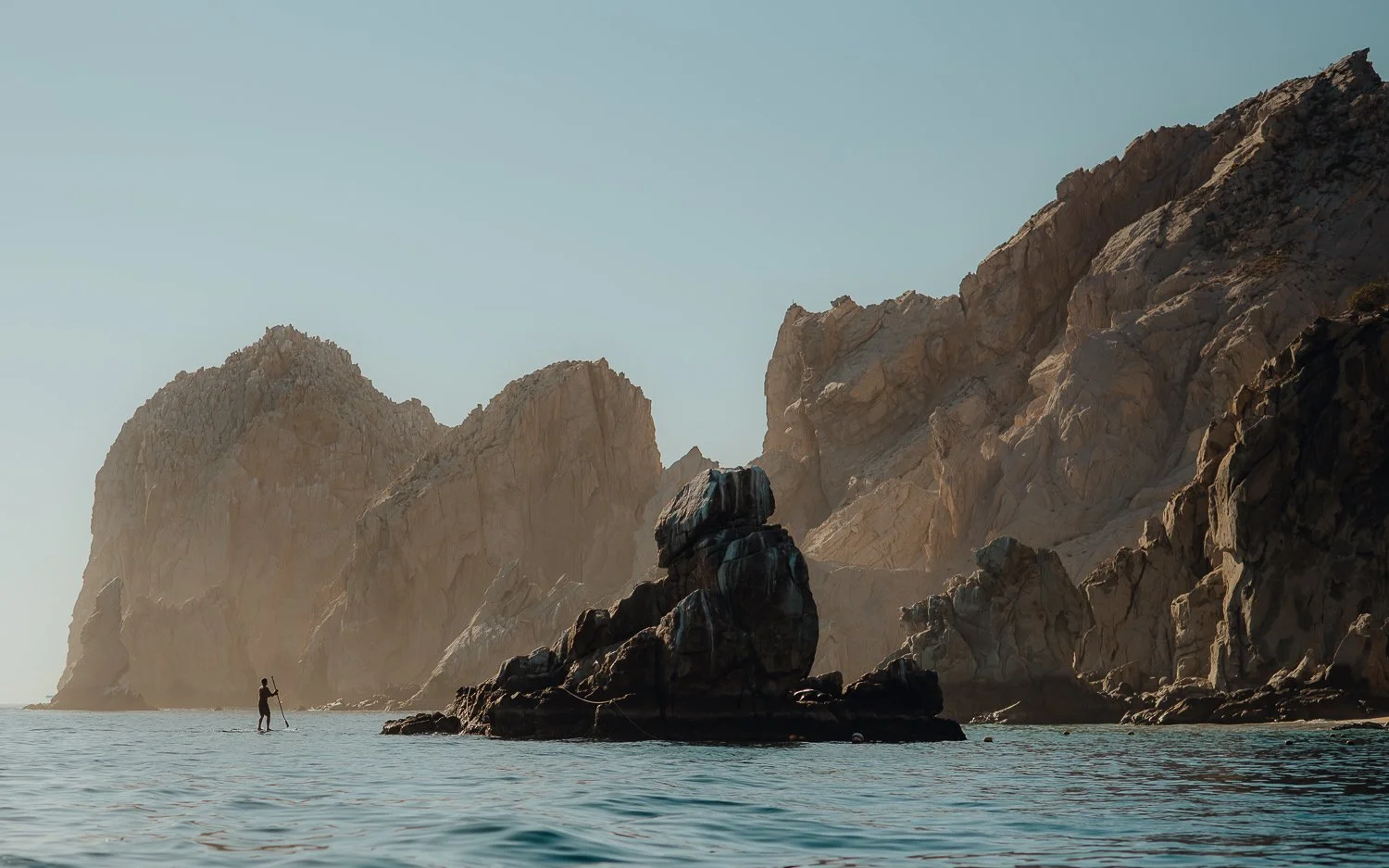 Adventure photography of man paddle boarding to unique rock formations at Lover's Beach in Cabo San Lucas, Mexico