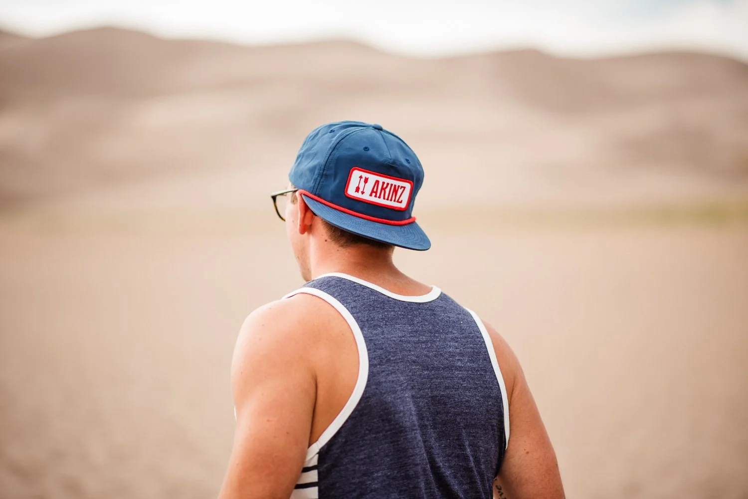 Adventure lifestyle product photography of a guy wearing a backwards blue snapback and bro tank in Great Sand Dunes National Park in Colorado for Akinz Boardwear