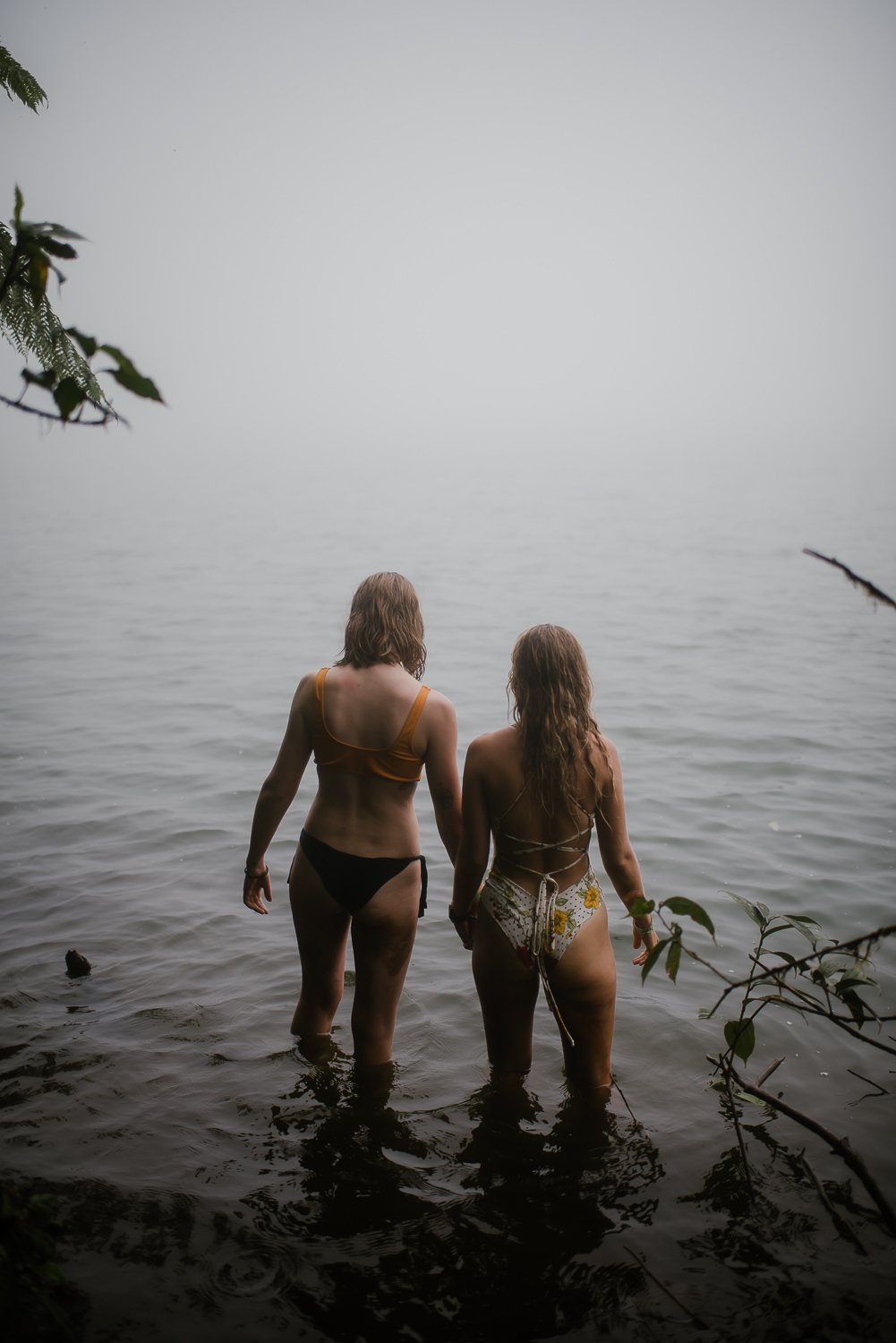 Travel portrait photograph of two girls wading into the foggy lake at the top of Cerro Chato in Costa Rica
