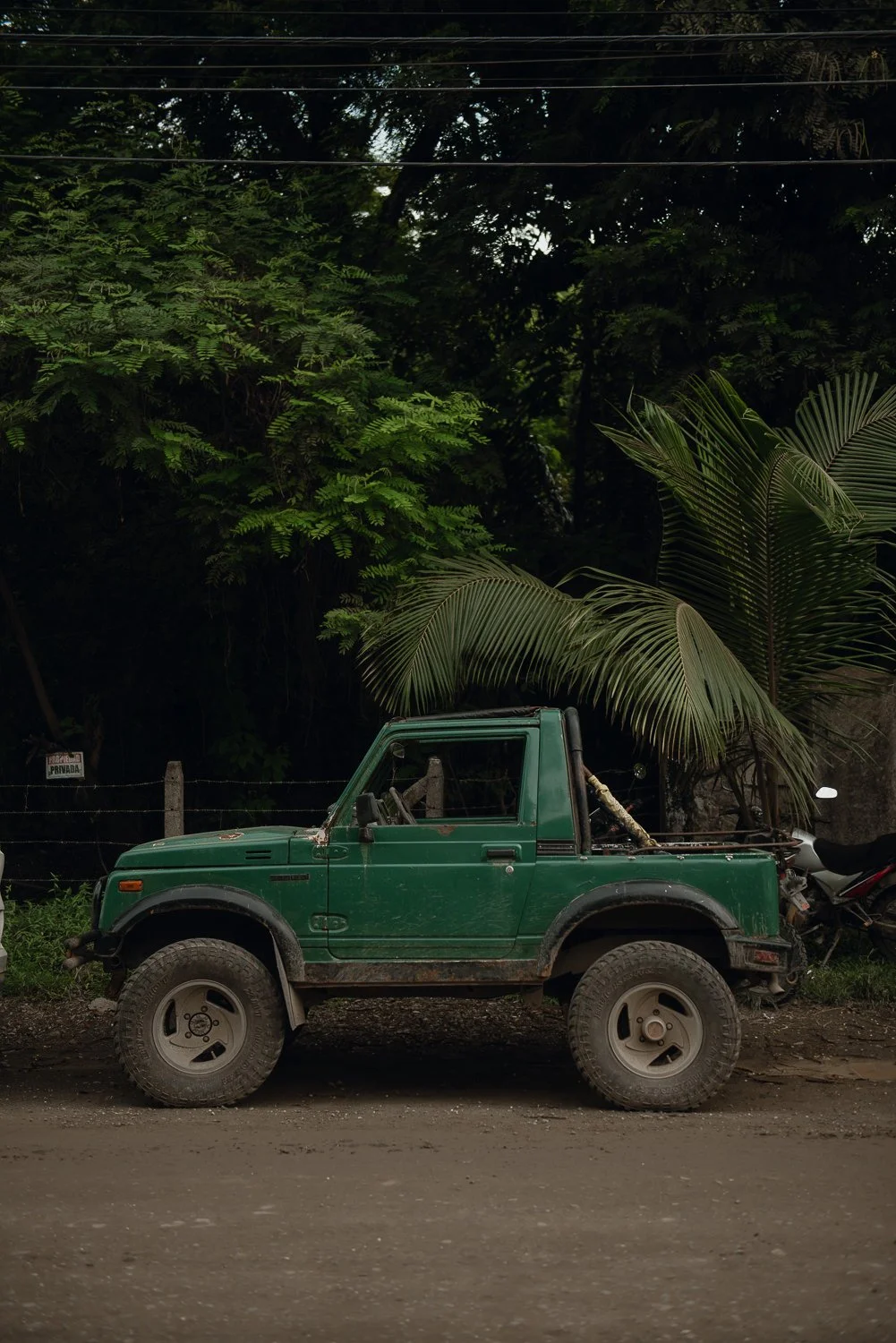 Small forest green Jeep like car parked in front of rainforest in Costa Rica