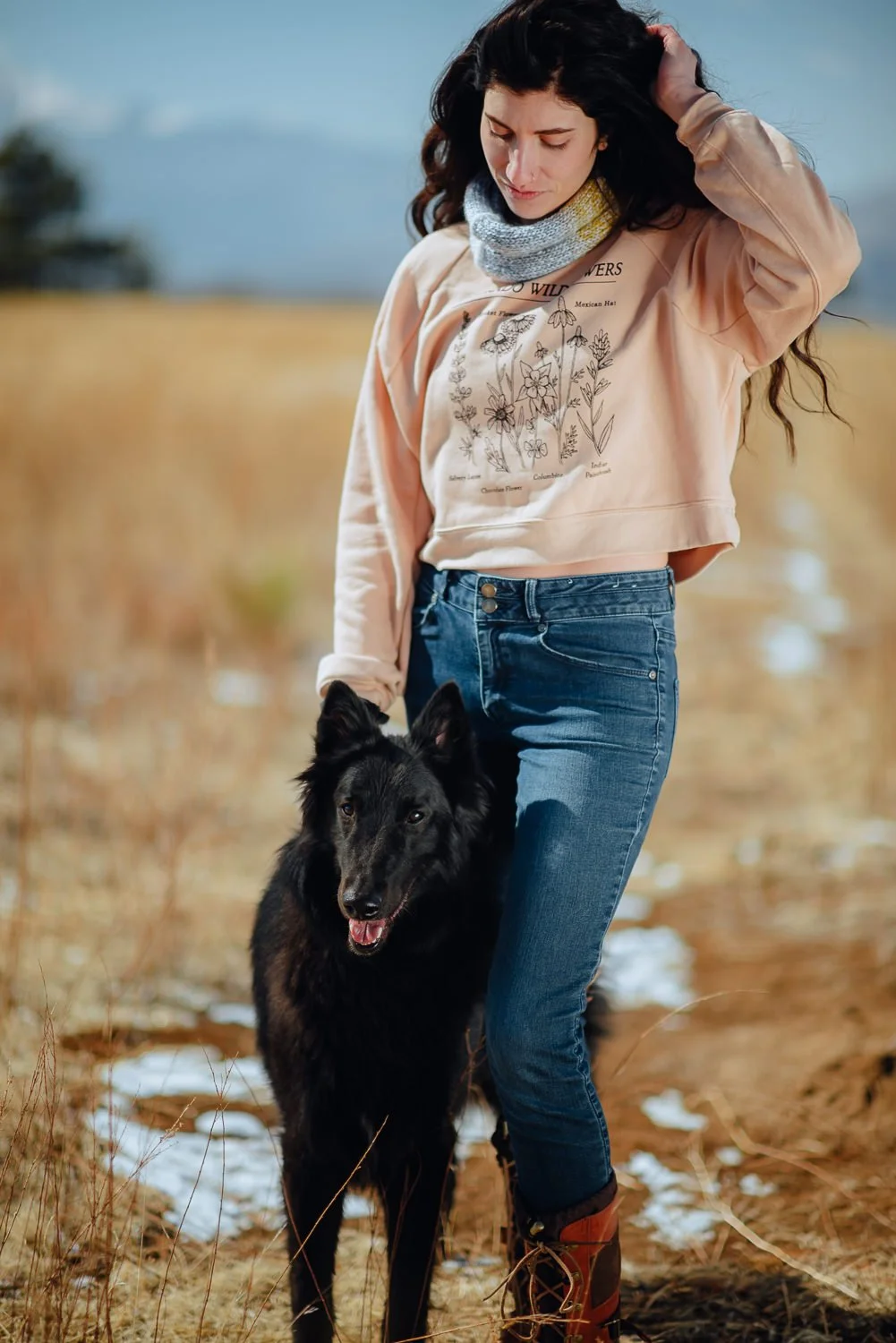 Lifestyle photography of young girl with long dark wavy hair wearing a peach wildflower crewneck sweater with her black dog at Palmer Park in Colorado Springs, Colorado for Akinz Boardwear