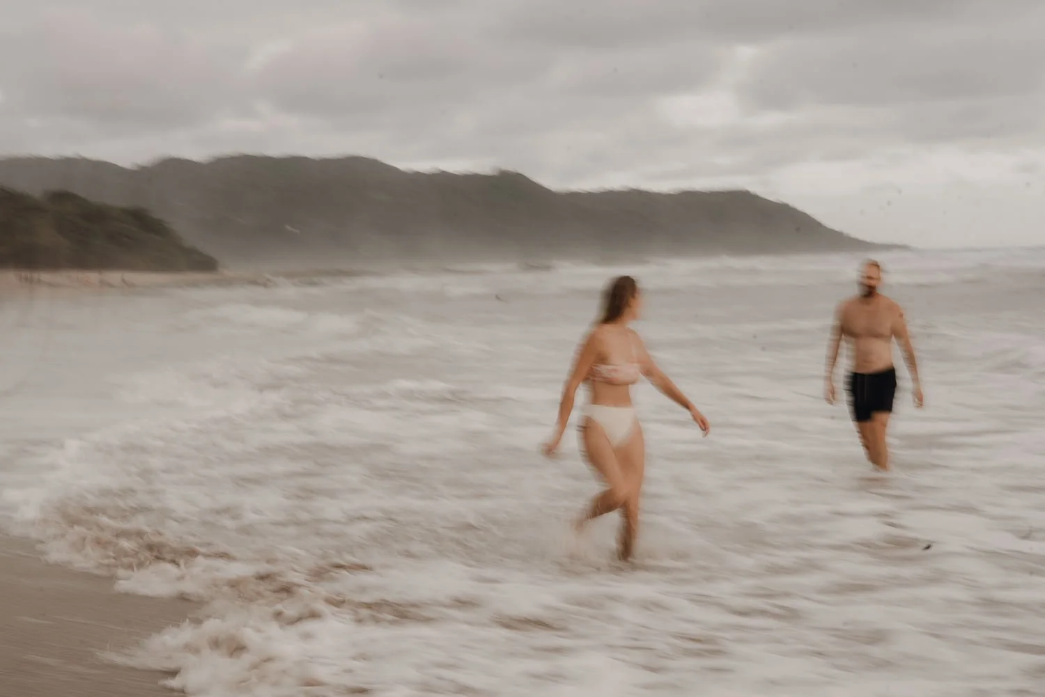 Slow shutter speed travel image of cute couple wading through waves on Santa Teresa shore in Costa Rica