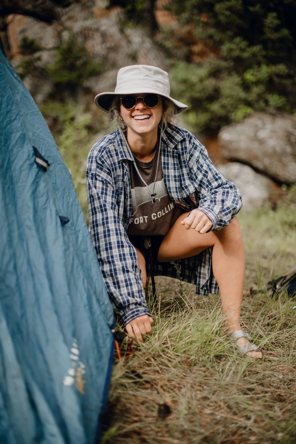 Adventure lifestyle photography of a cute blonde girl in a bucket hat pitching a tent while camping in Northern Colorado for Akinz Boardwear