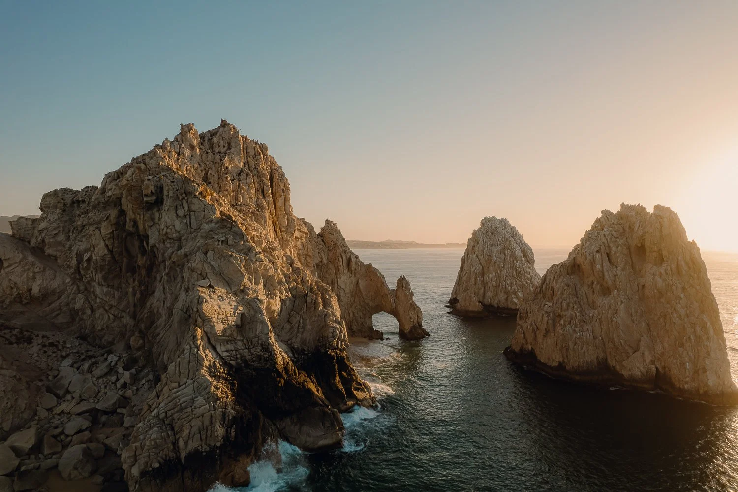 Travel drone photography of the famous Arch and other rock formations during golden hour sunrise at Lover's Beach in Cabo San Lucas, Mexico