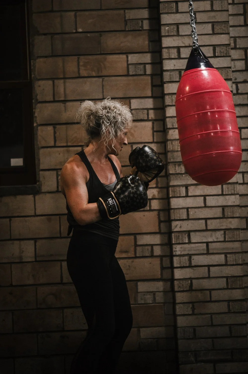 Lifestyle photograph of a woman hitting a red punching bag at Beautifully Savage boutique boxing gym in Fort Collins, Colorado