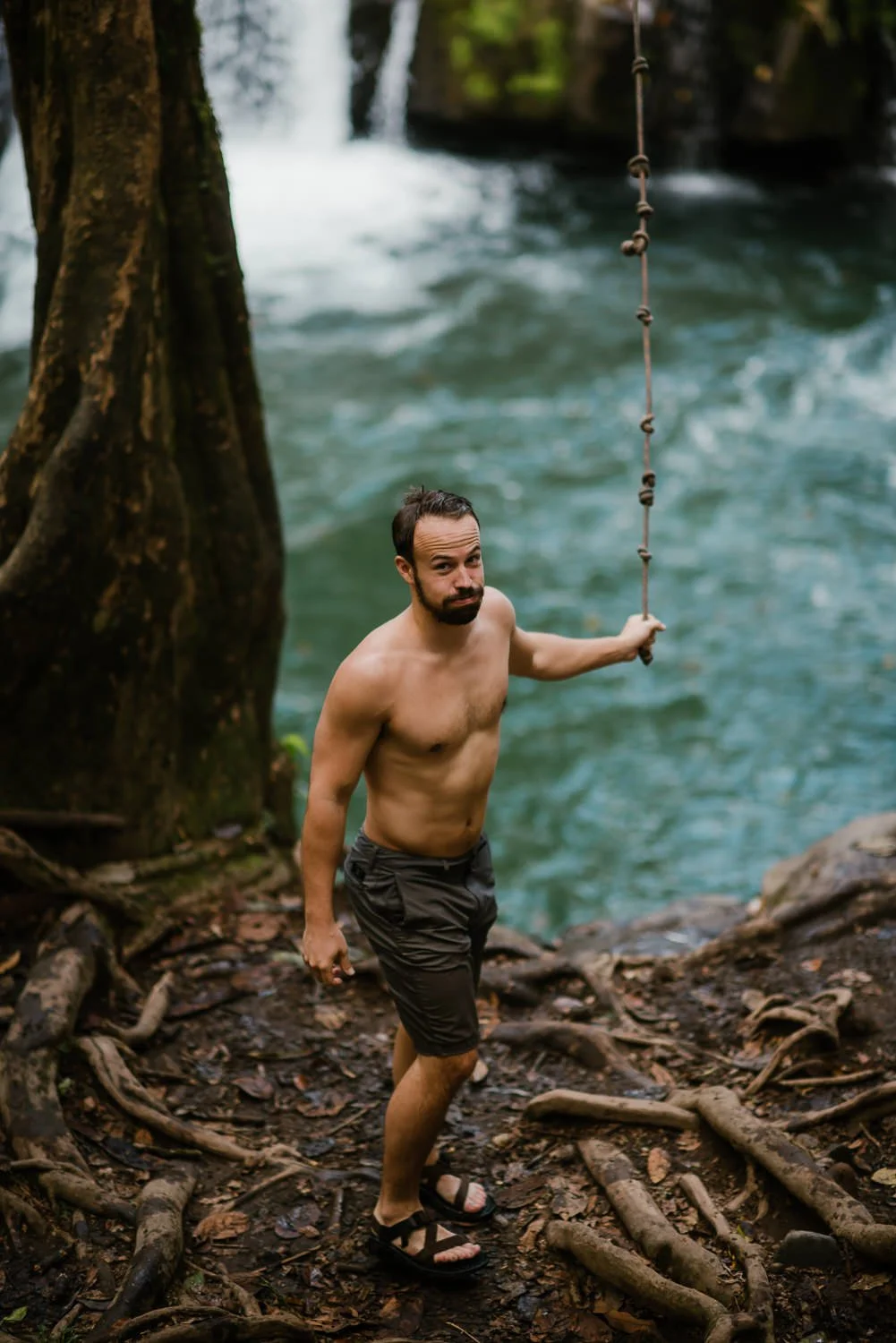 Travel photograph of a young man rope swinging into a river
