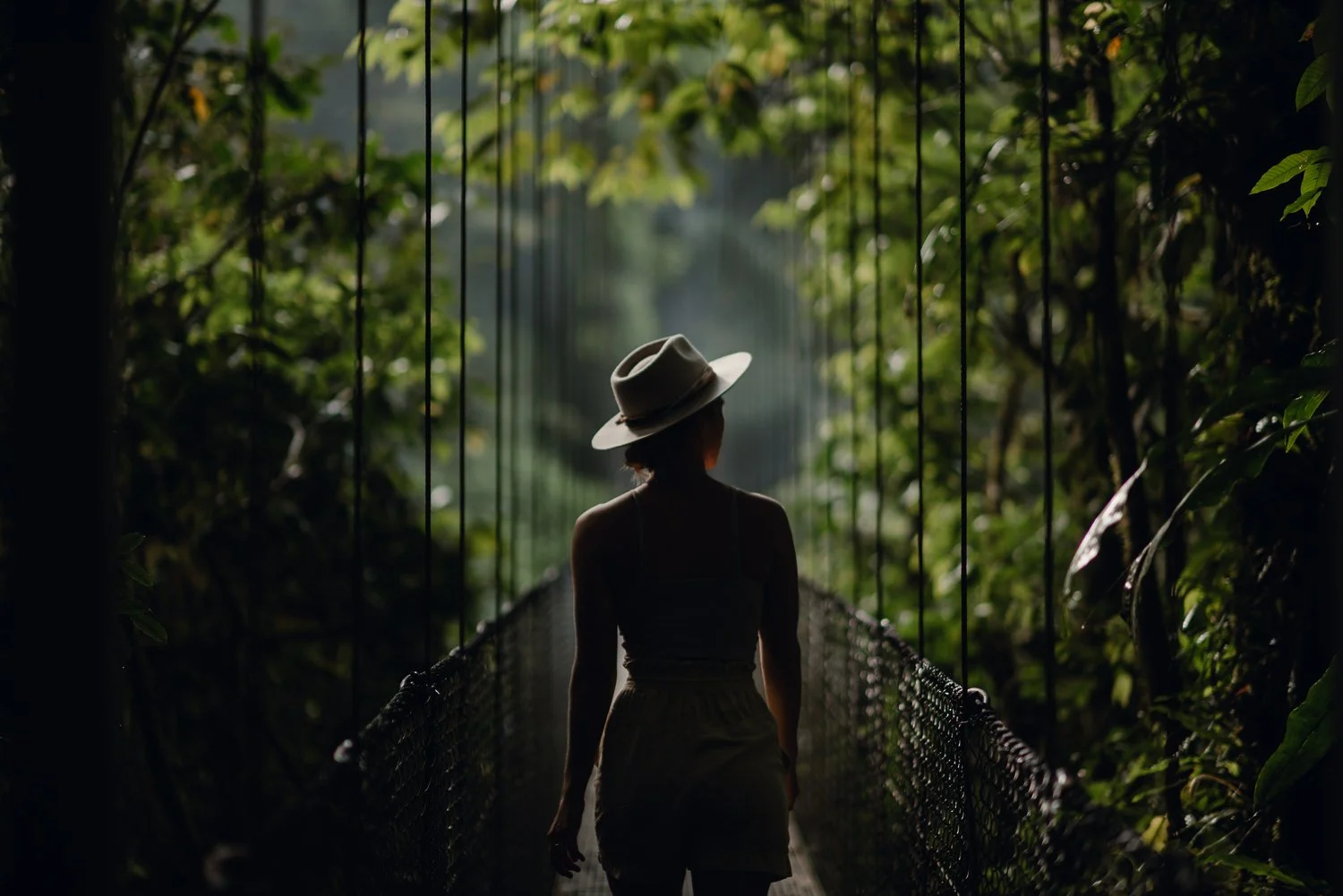 Lifestyle portrait of a girl wearing a hat, walking on a hanging bridge in the cloud forest in La Fortuna, Costa Rica