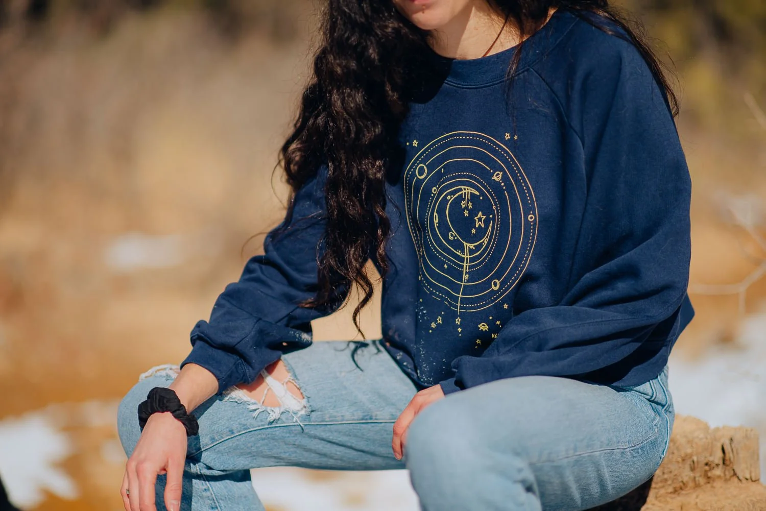 Professional lifestyle photography of young model with long brown hair wearing a dark blue Akinz Boardwear sweatshirt in the snowy mountains in Colorado Springs, Colorado