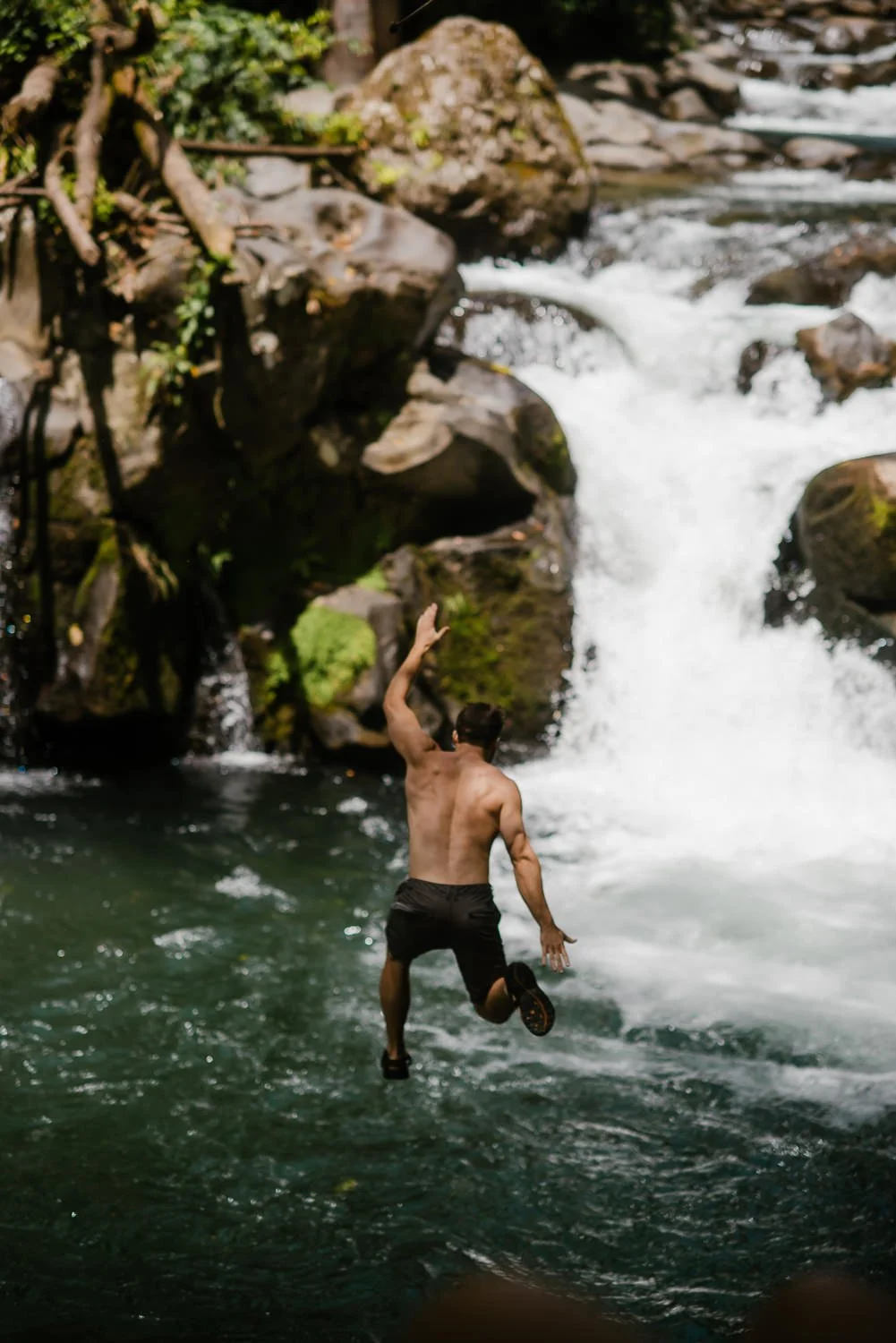 Travel photograph of a young man rope swinging into a river