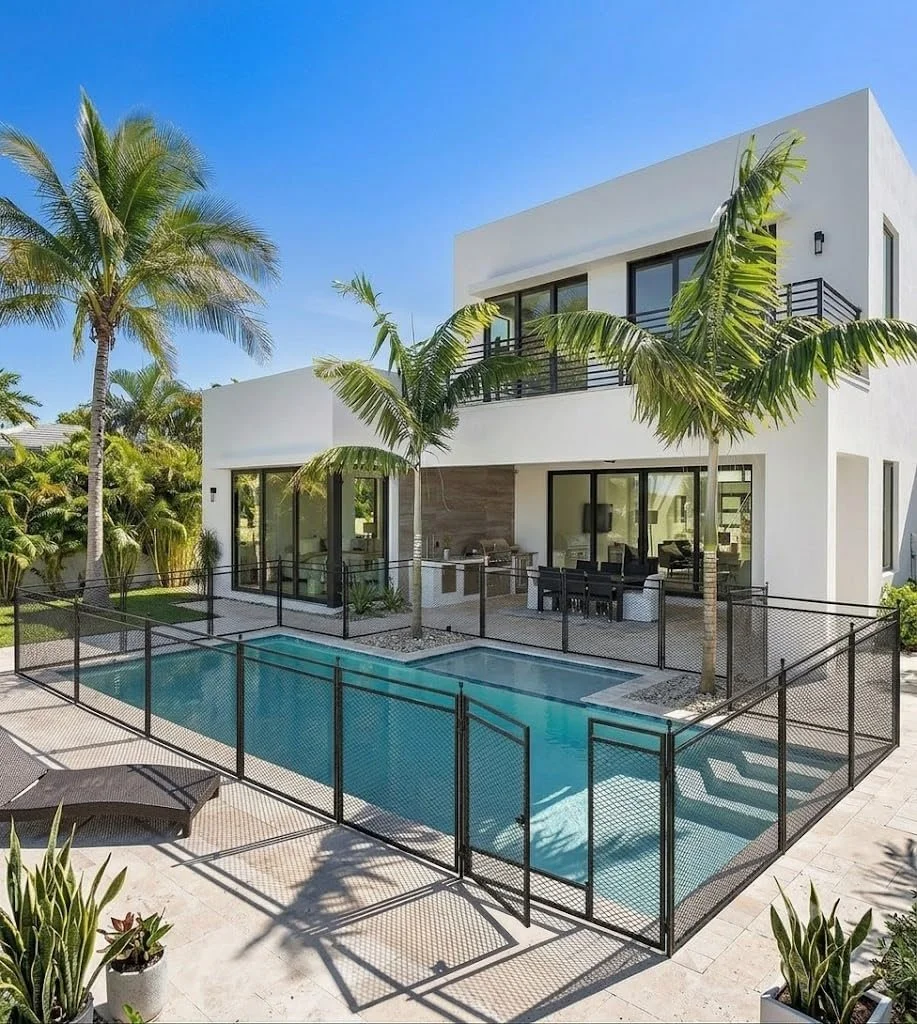 A backyard with a swimming pool, a safety fence around the pool, and a grassy yard area.