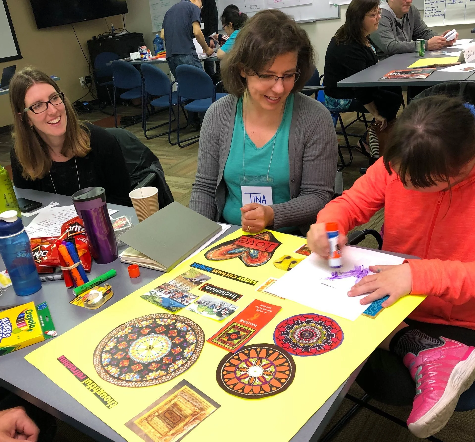Mother and young daughter creating a poster with another lady looking on.  All are smiling.