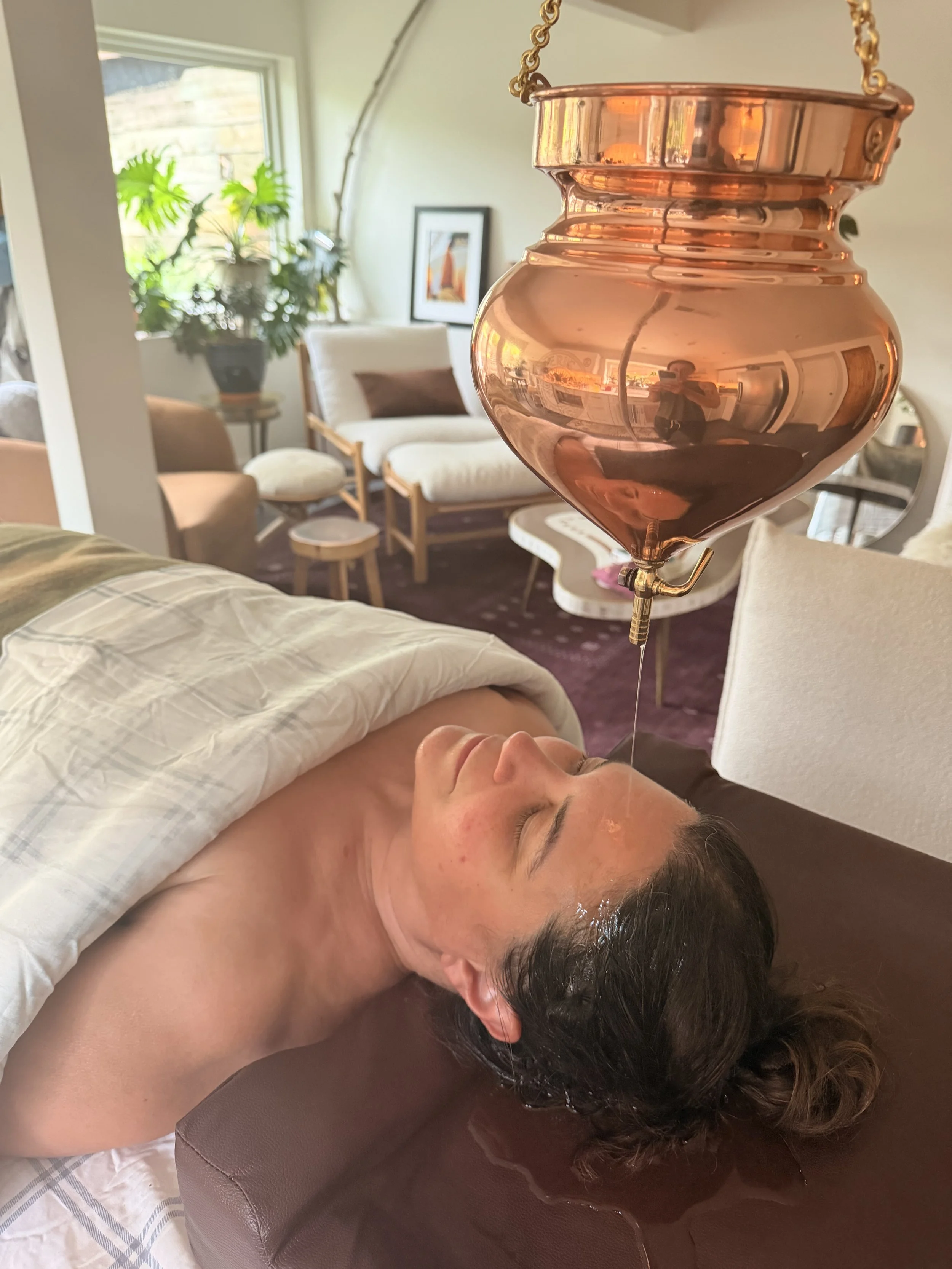 Traditional Shirodhara oil treatment using a copper vessel during an Ayurvedic consultation in a holistic wellness clinic