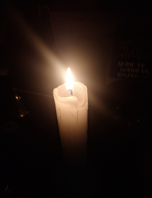 A white candle lit and with runes carved into the sides in the dark.
